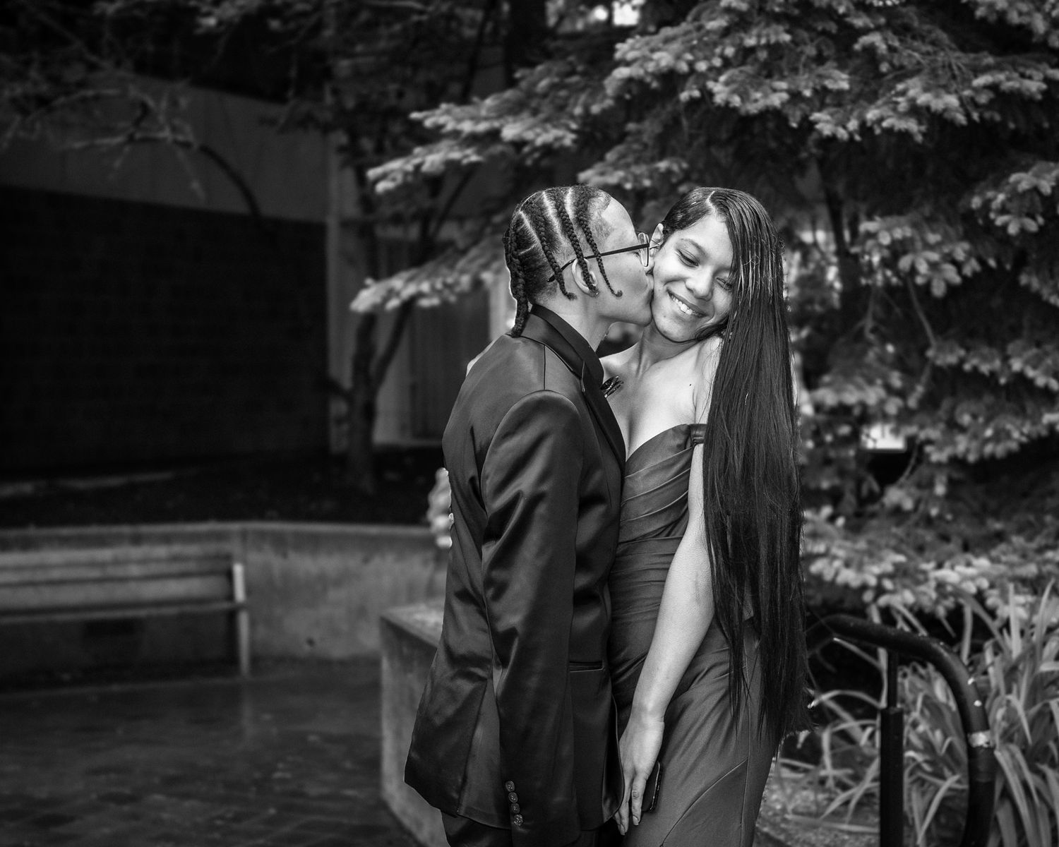 A black and white romantic moment between a couple embracing outdoors with lush trees in the background.