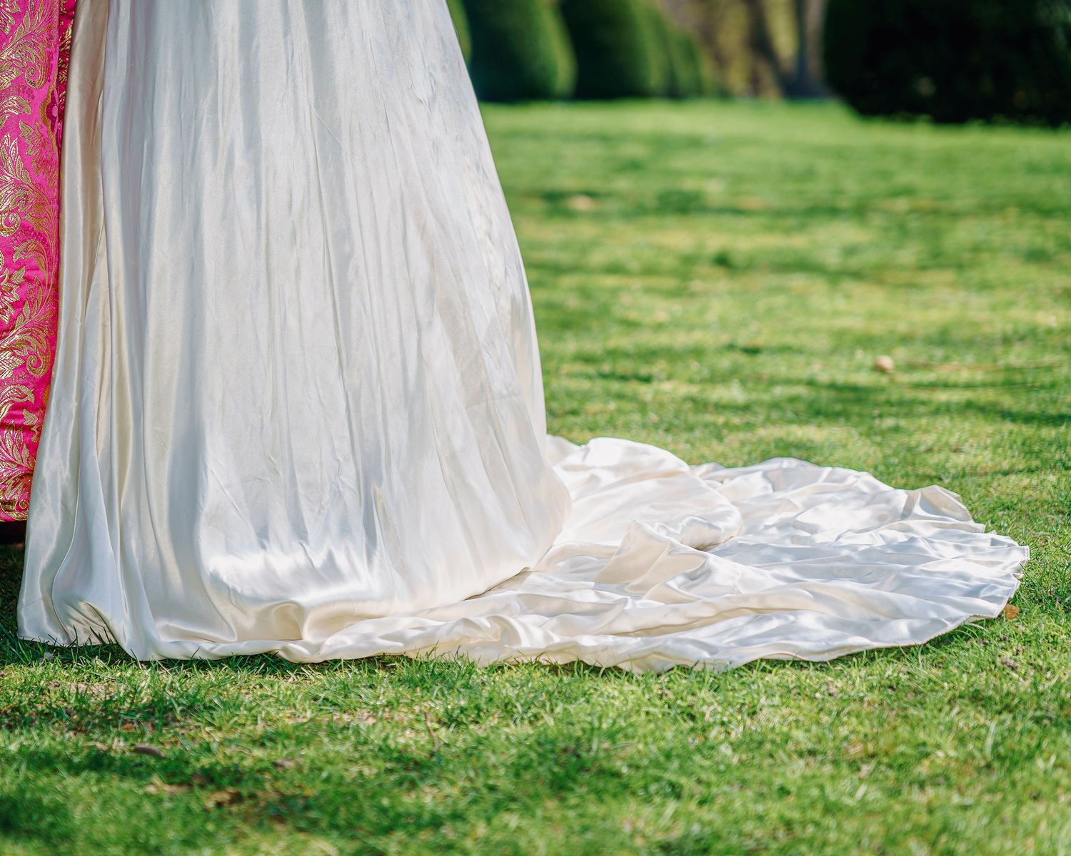 Elegant white wedding dress train flowing across green grass lawn on sunny outdoor day.