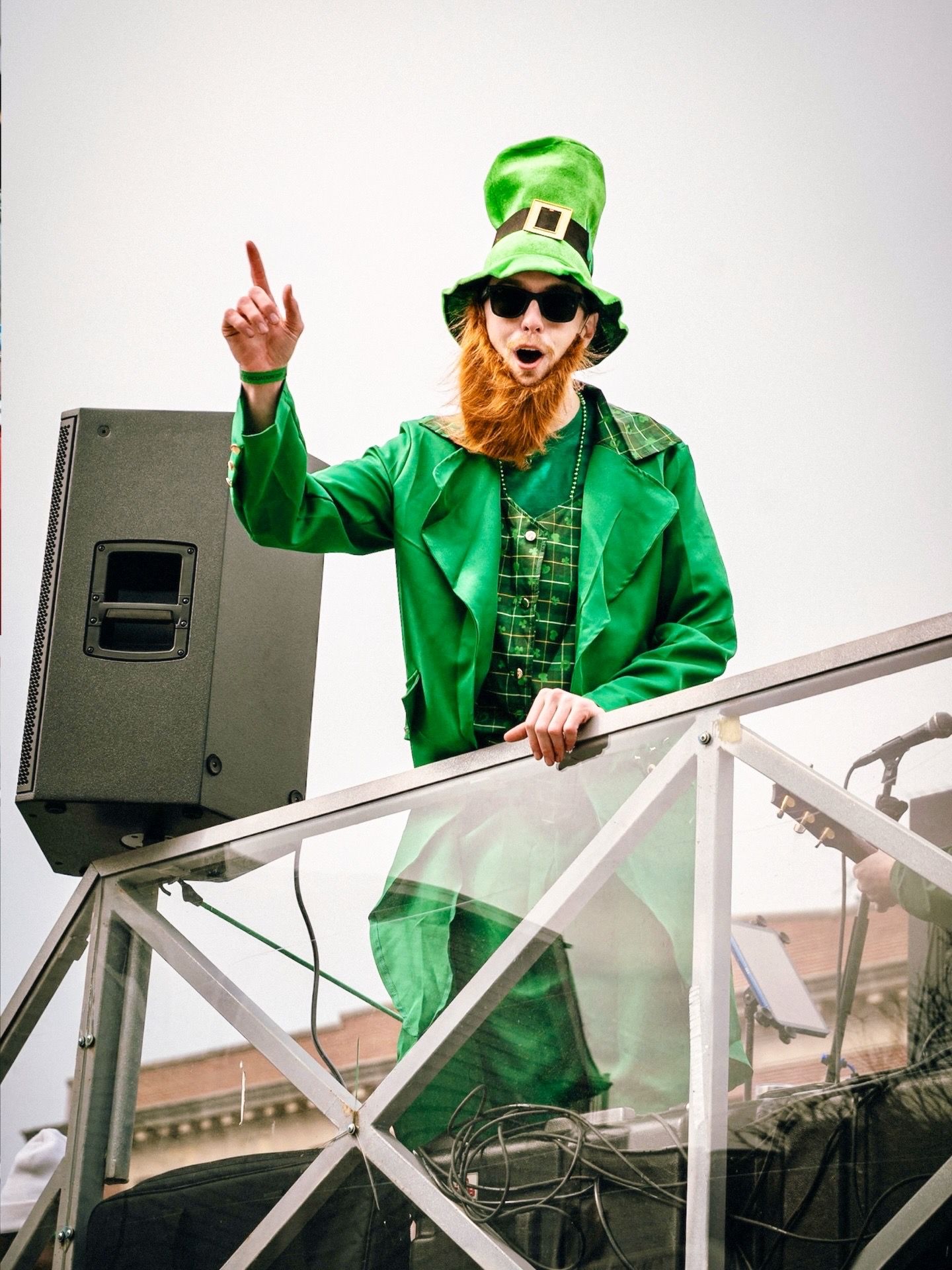 A figure in a bright green St. Patrick's Day outfit and ginger beard dances energetically on a stage platform.