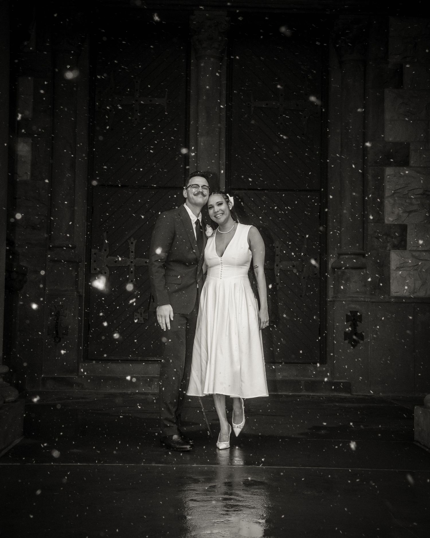Elegant couple stands in doorway while snow falls creating a romantic atmosphere. Boston elopement & intimate wedding photography.