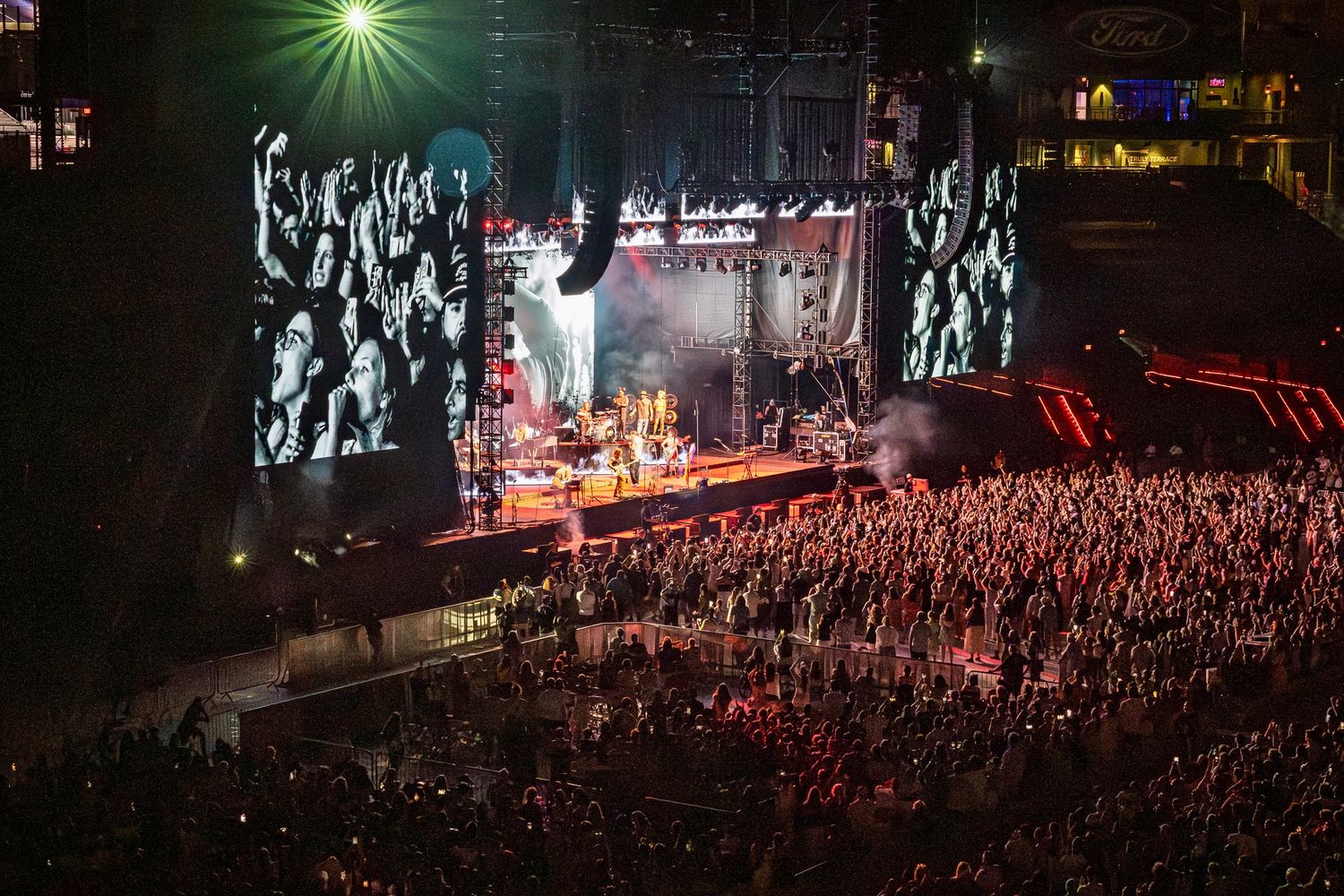 Concert crowd silhouetted in front of illuminated stage with dramatic lighting effects during nighttime performance.