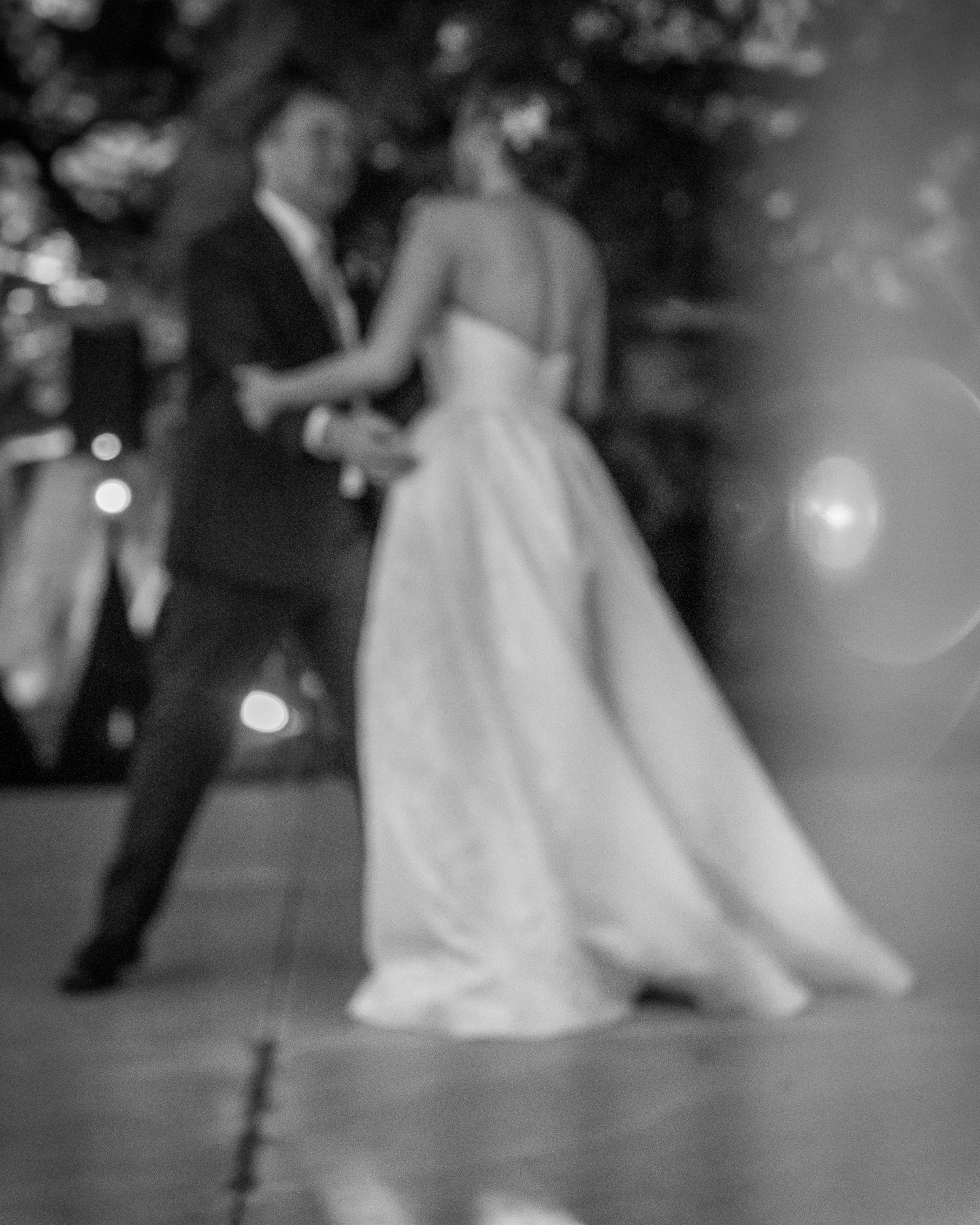 A couple shares their first dance at a wedding reception captured in dreamy black and white photography.