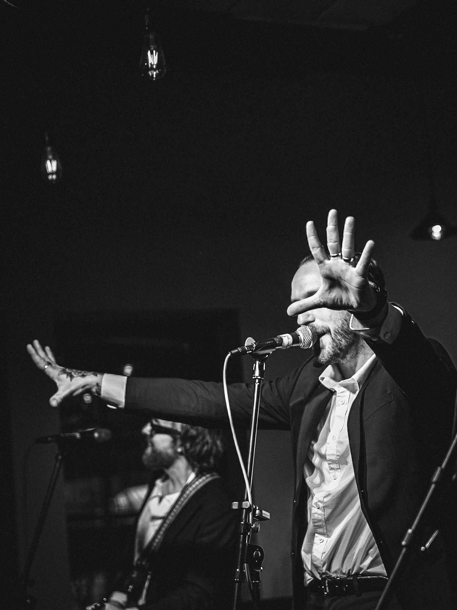 Black and white photo of two male musicians performing on stage, one raising his hand near a microphone.
