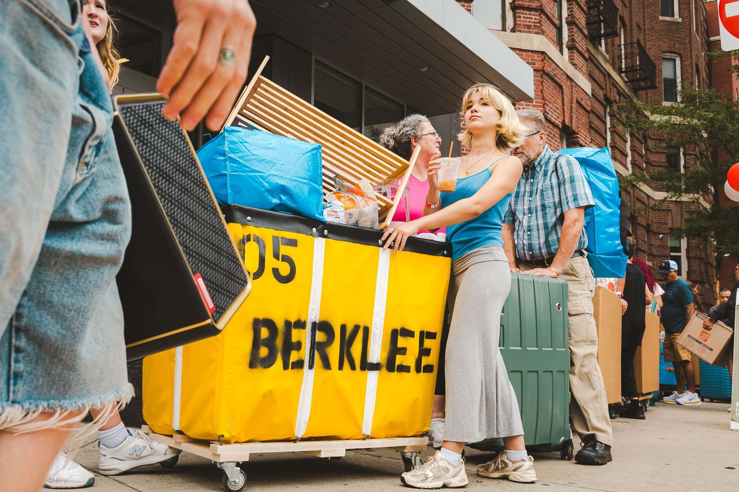Students moving into Berklee College of Music dorms, loading belongings onto a yellow cart on a busy city sidewalk.