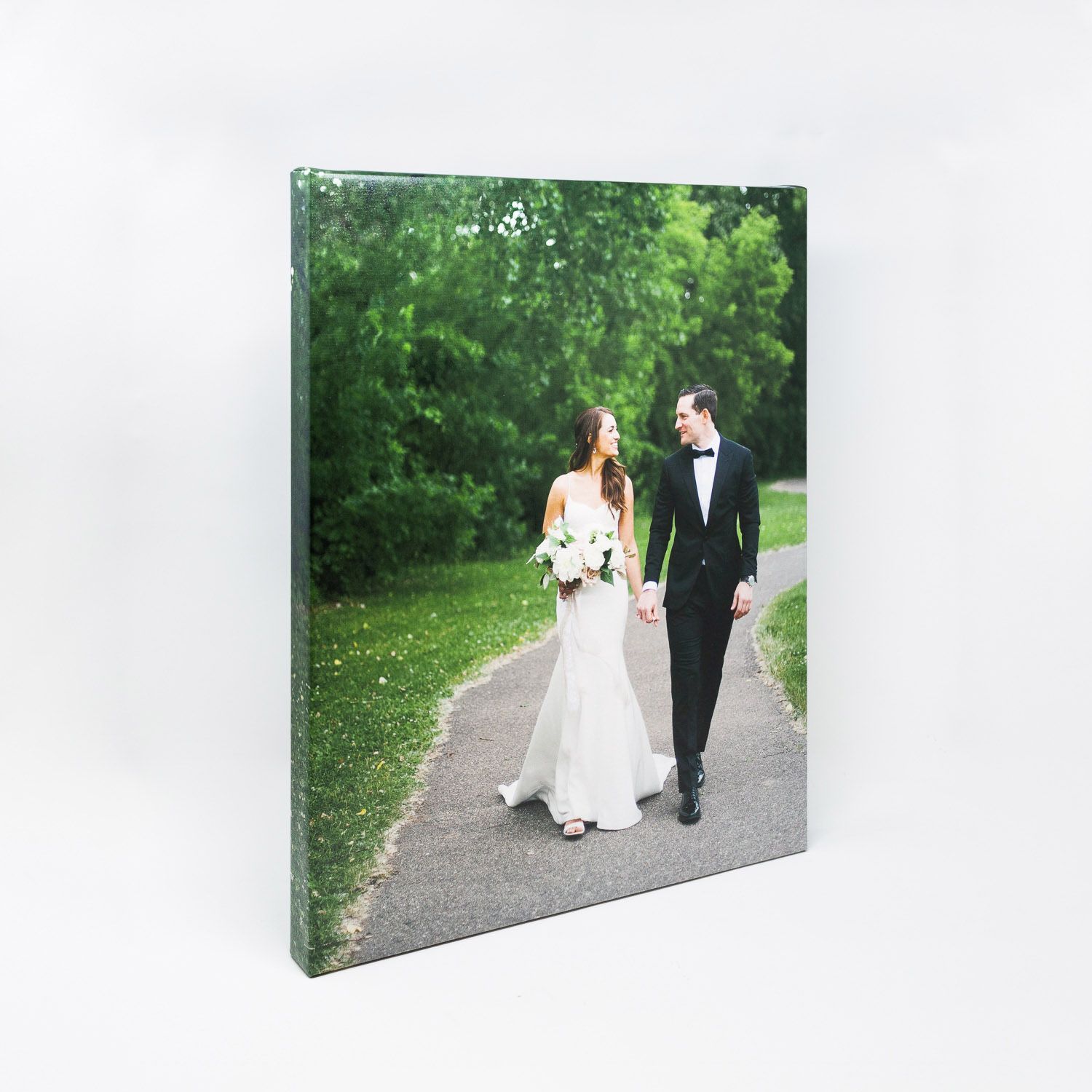 A couple in formal wedding attire walking down a tree-lined path together on their special day.