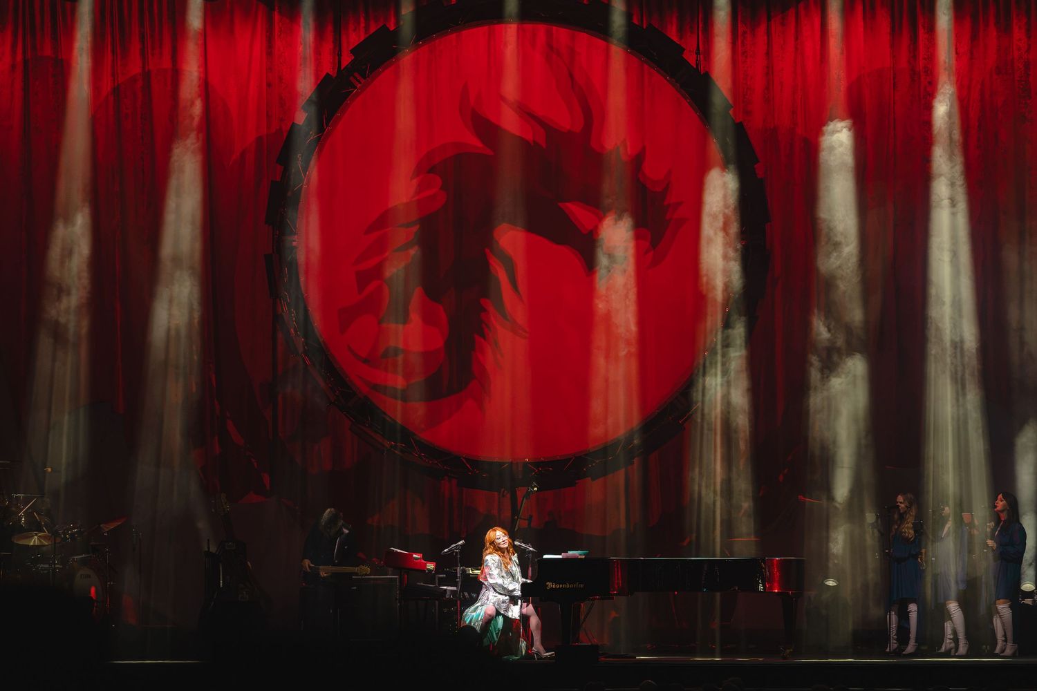 Performer on stage at piano with dramatic red dragon projection on curtain backdrop with spotlights.