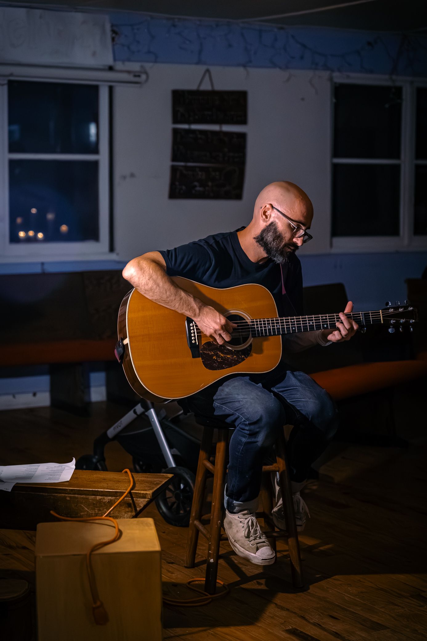 Musician plays acoustic guitar in dimly lit room during intimate recording session.