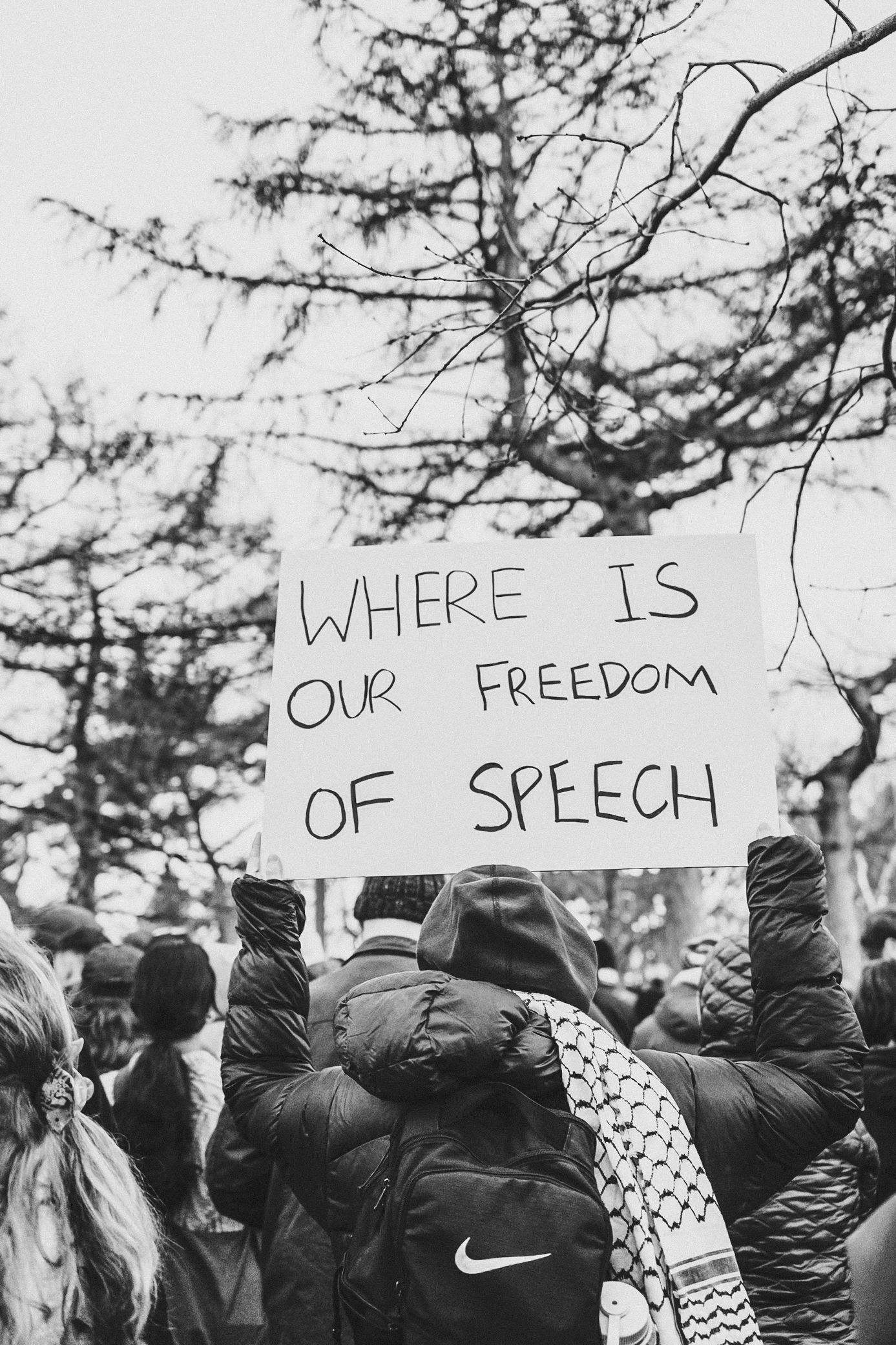 Protest signs held up against a winter sky asking about freedom of speech.