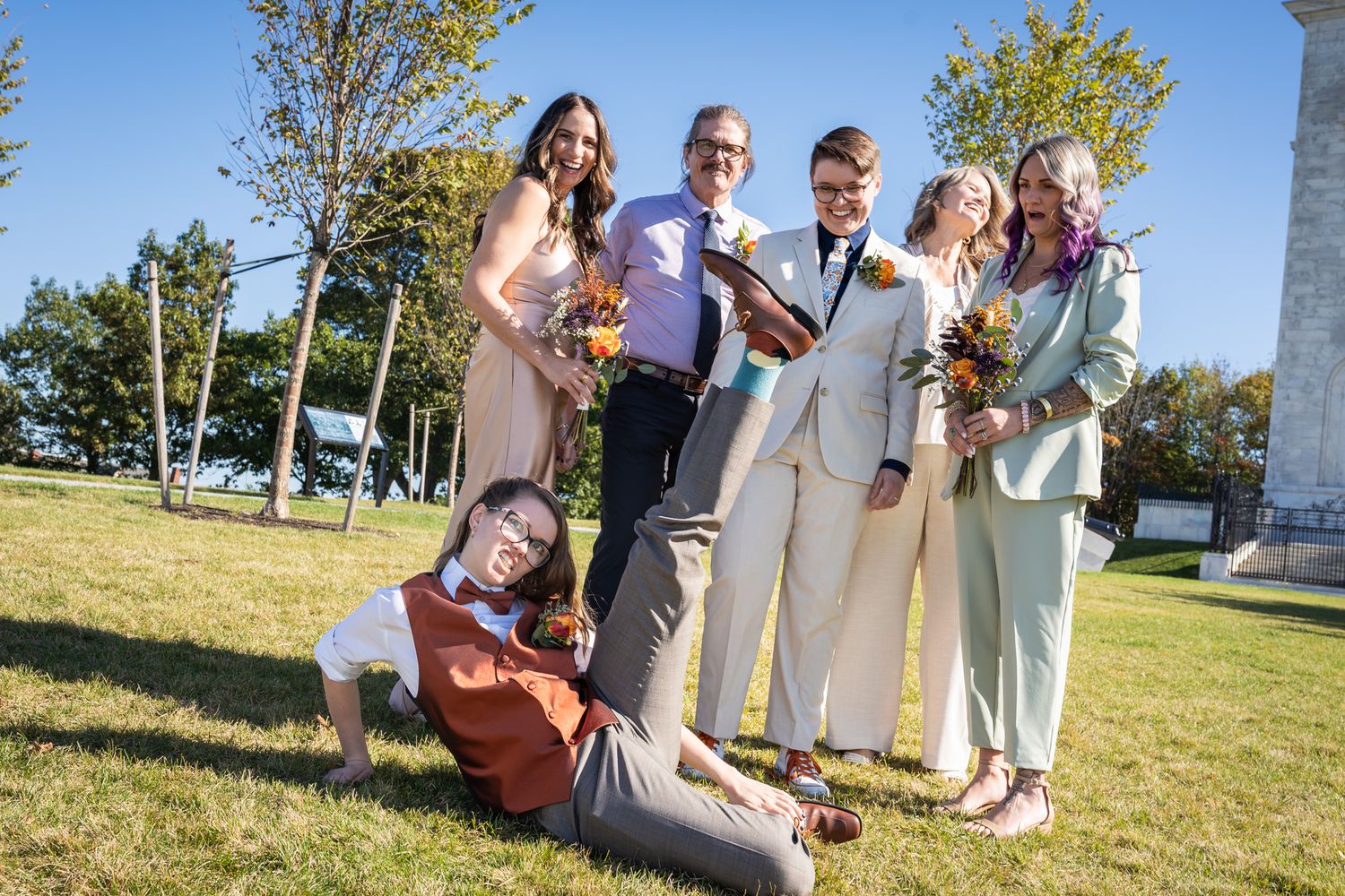 A group of people stand together outdoors on a sunny day enjoying a casual gathering in a grassy area.