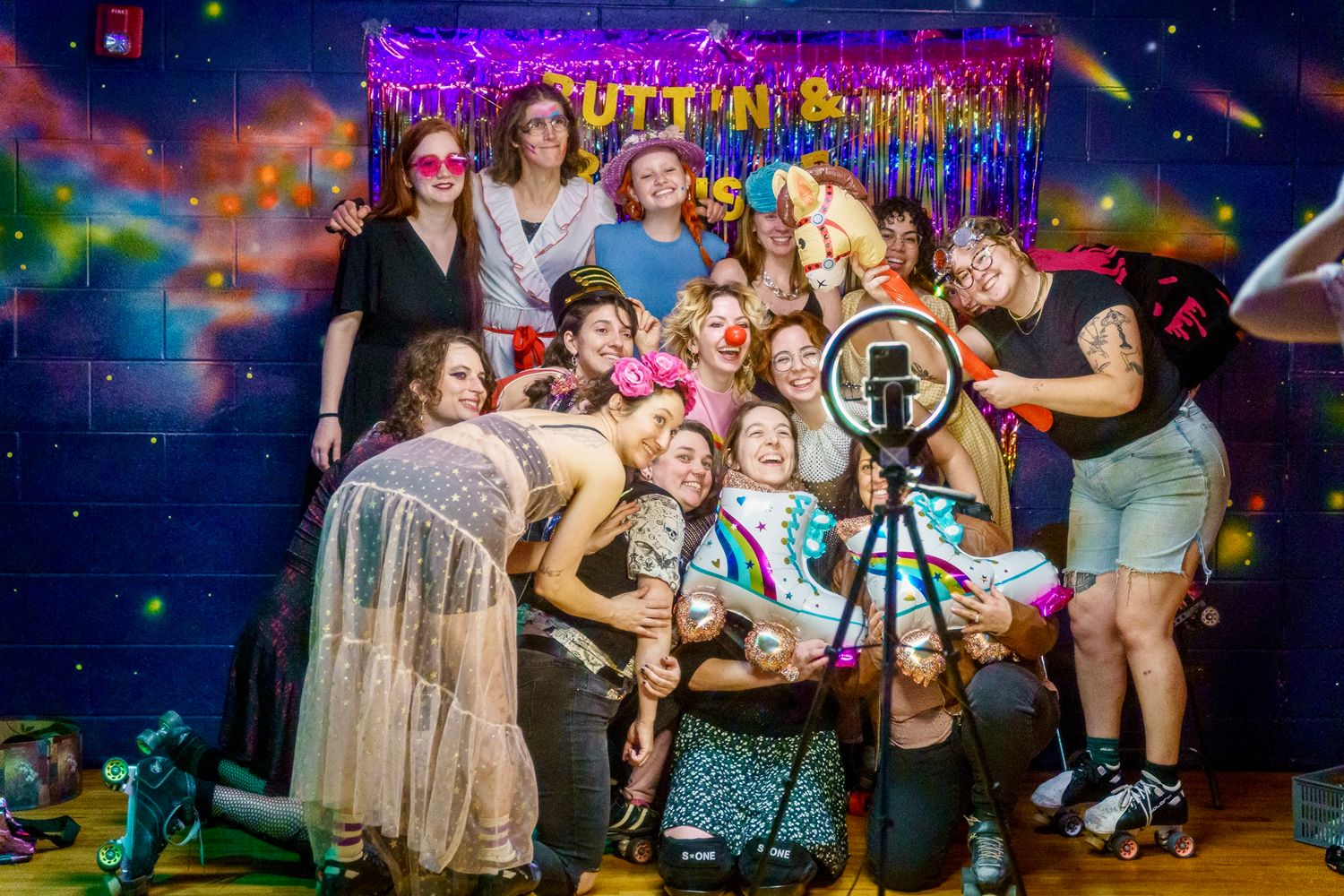 A group poses together at a party with purple decorations and a sparkly backdrop in what appears to be a celebration setting.