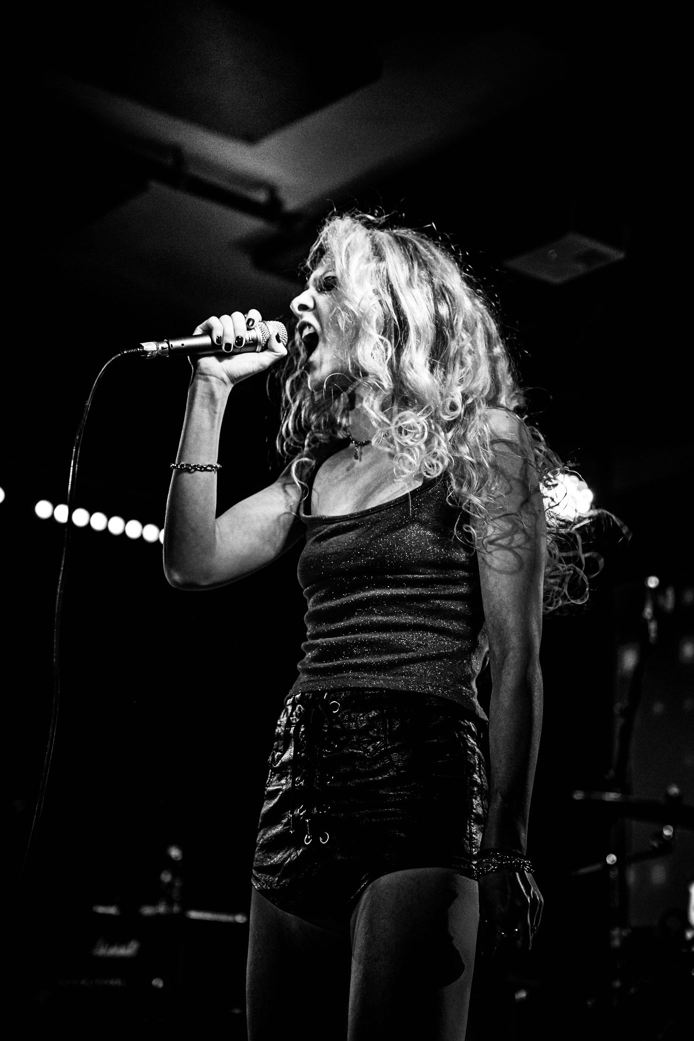 Black and white photo series of a performer singing passionately on stage in dark clothing at a concert venue.