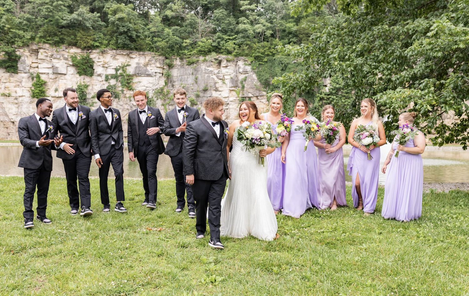 Wedding party members laugh and pose together during outdoor photo session in a garden setting.