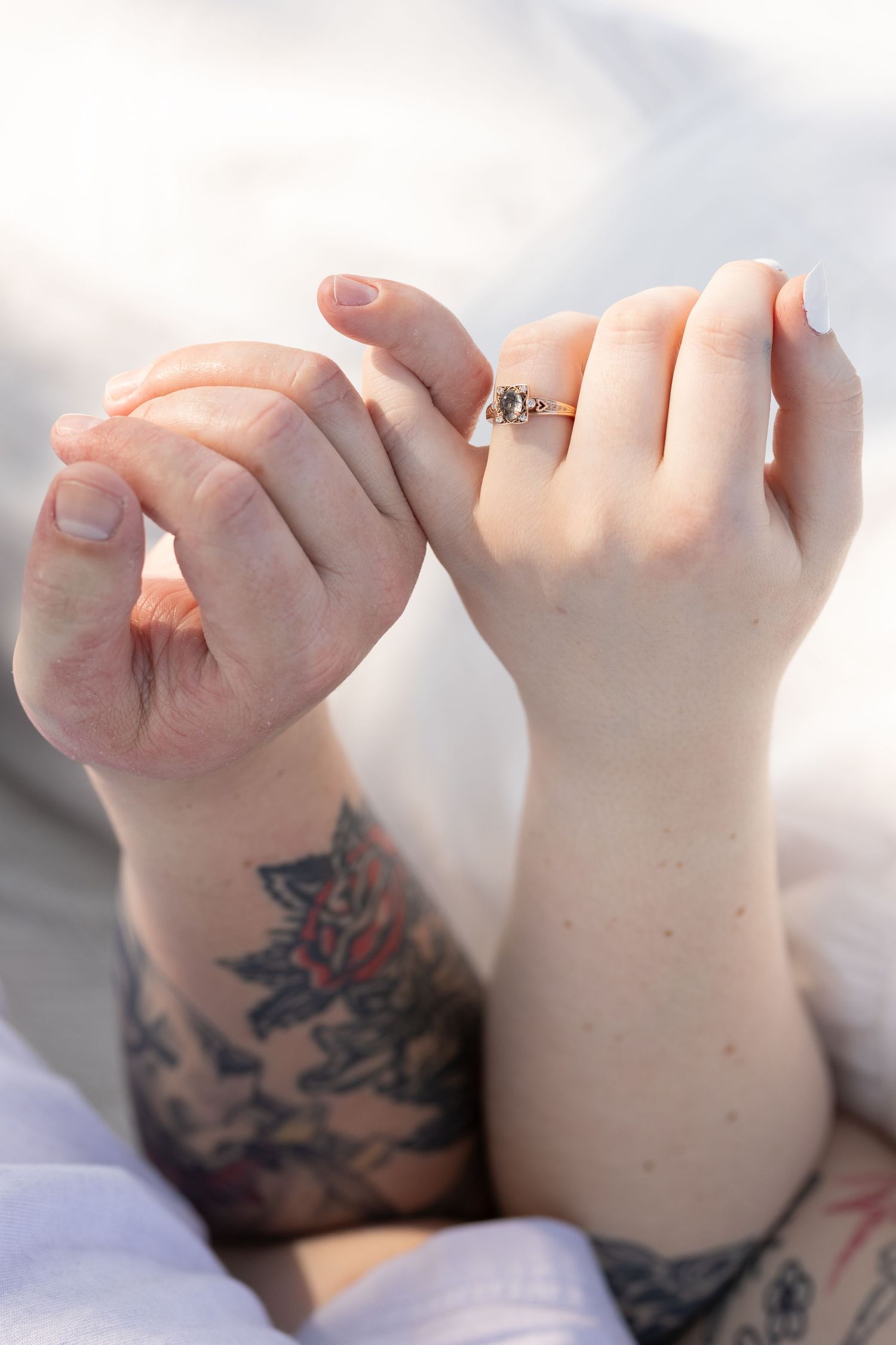 Close-up of interlocked hands showing engagement ring and floral tattoo.