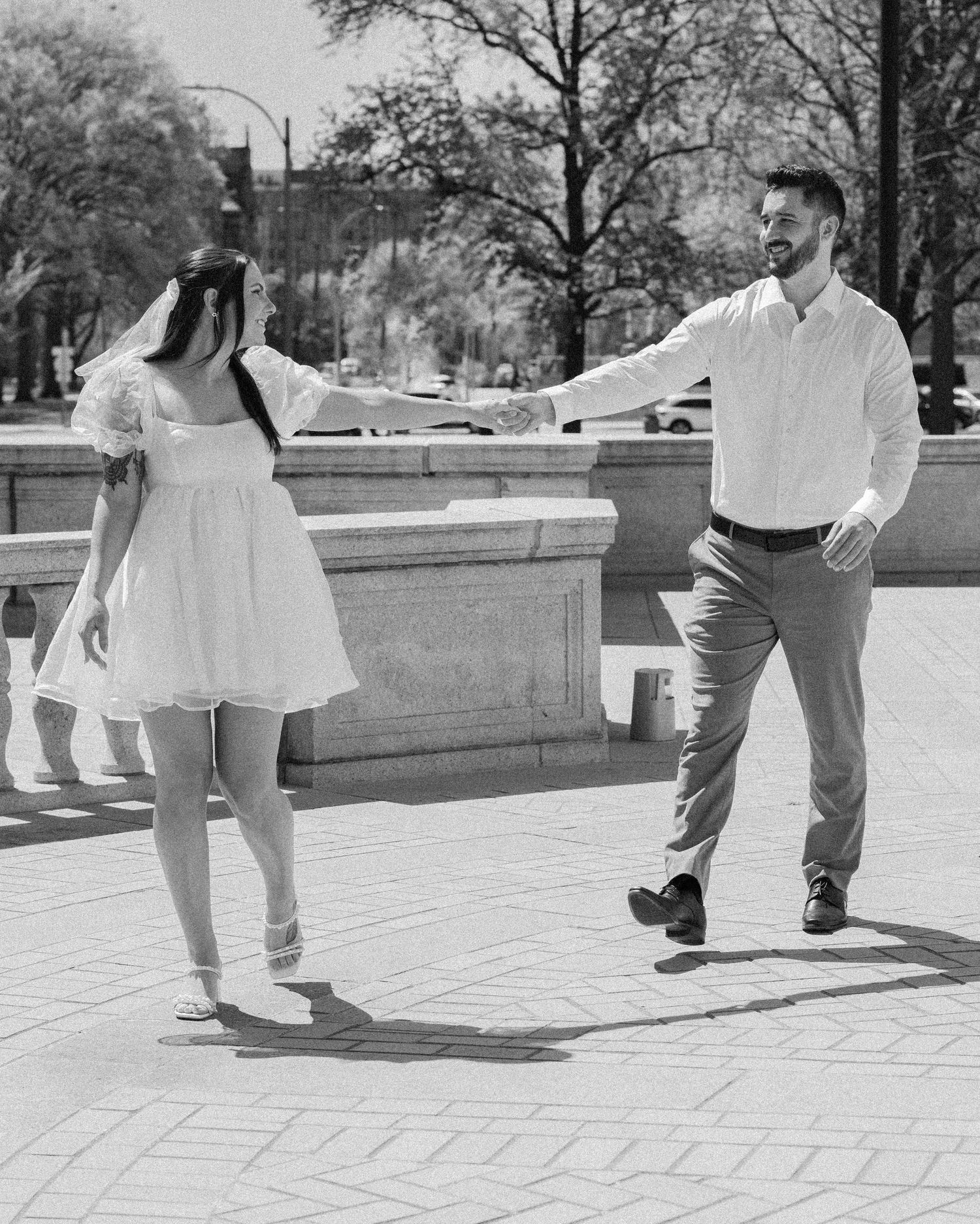 A black and white photo of a couple dancing playfully in an outdoor urban setting.