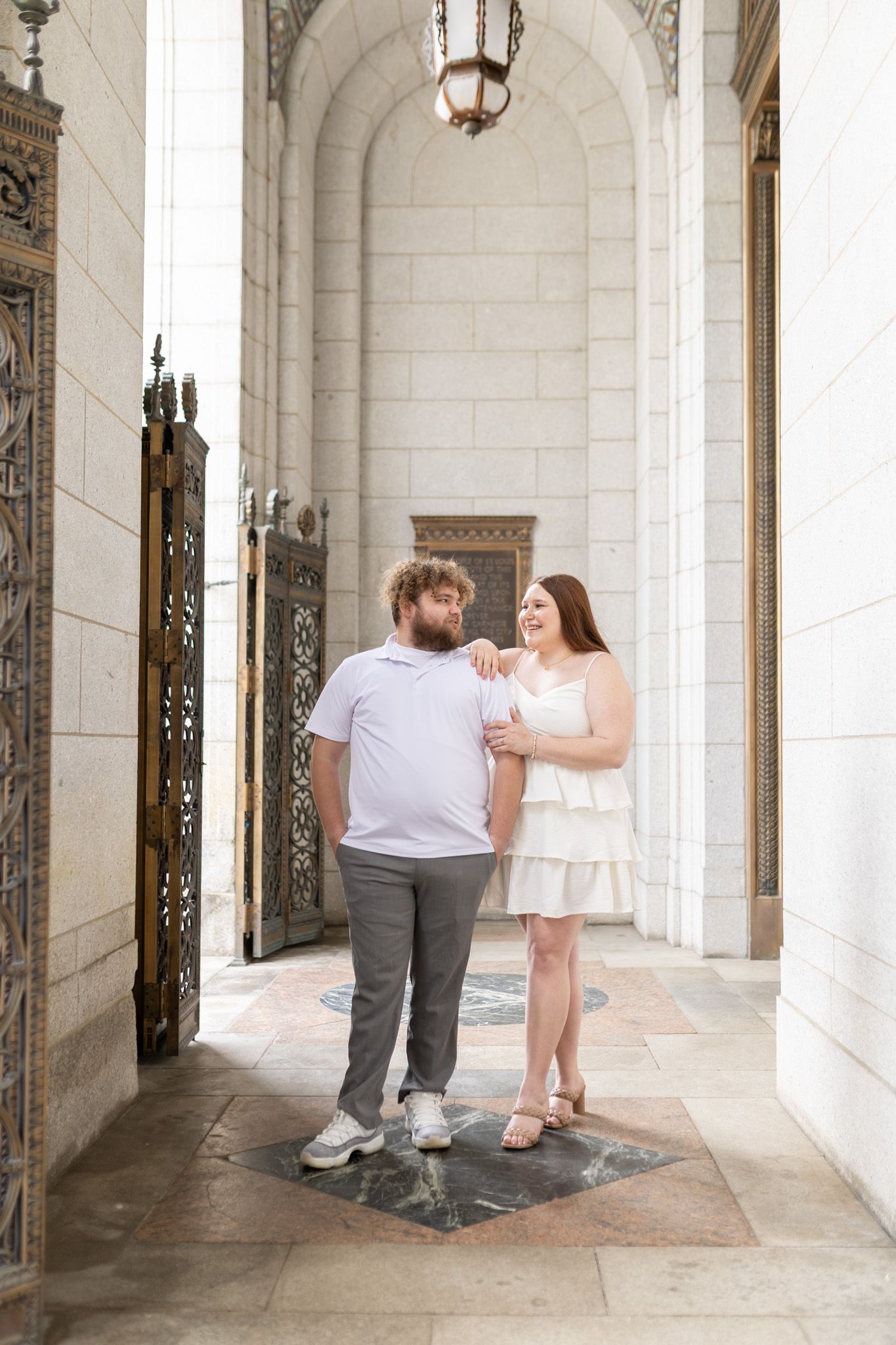 A couple stands together under an elegant architectural archway with ornate gates.
