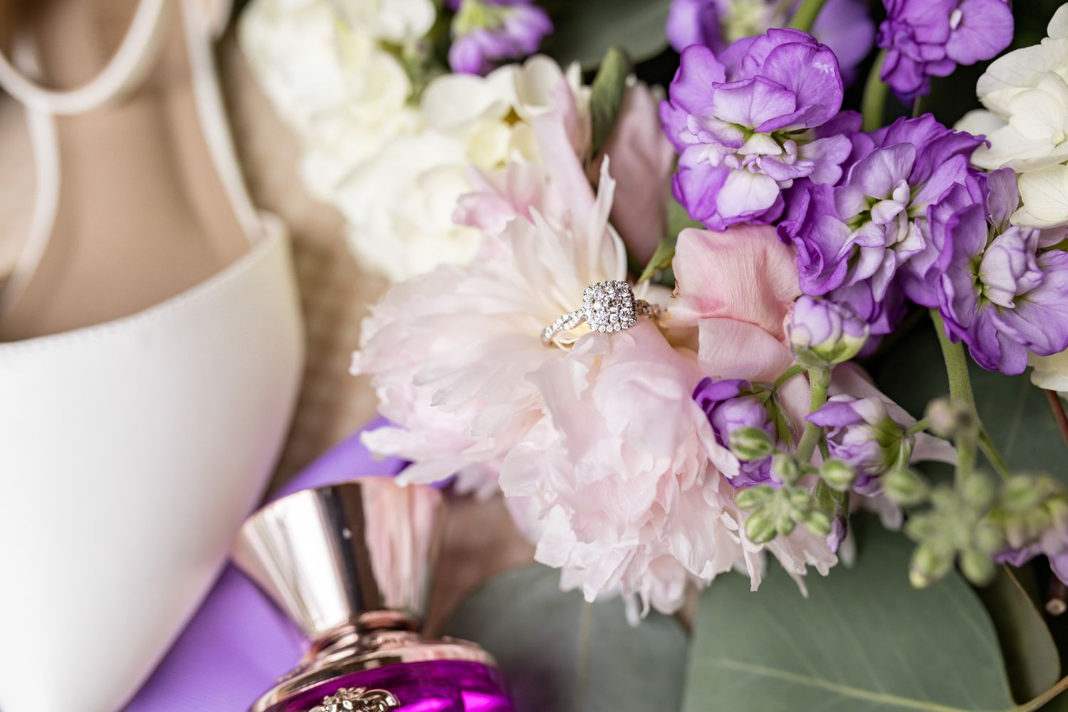 Purple and pink floral wedding bouquet arranged with white roses and delicate blossoms against a soft neutral background.