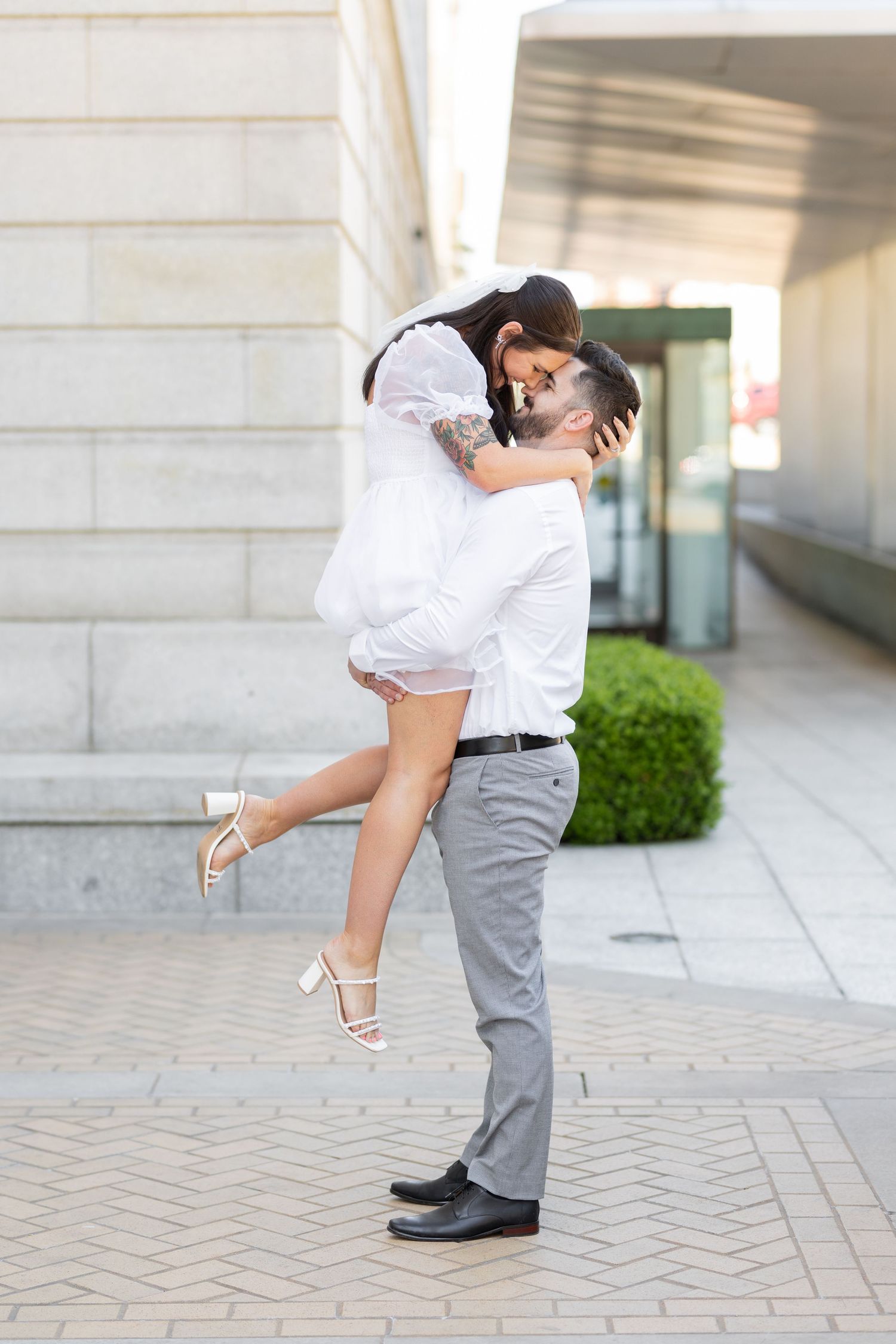 A romantic couple embracing in a playful pose against a light colored building exterior.