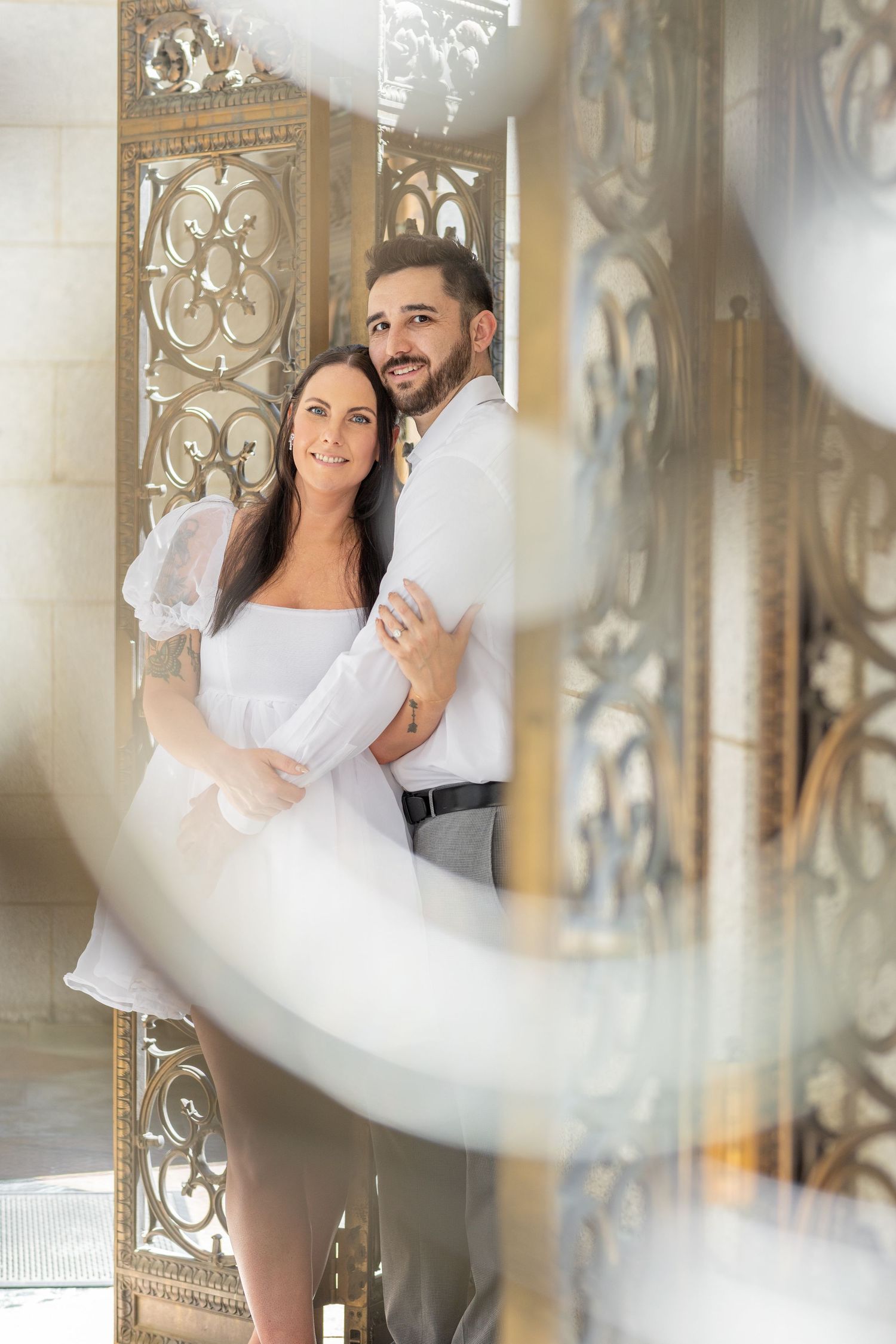 A romantic couple embraces near decorative gold panels in an elegant indoor setting.