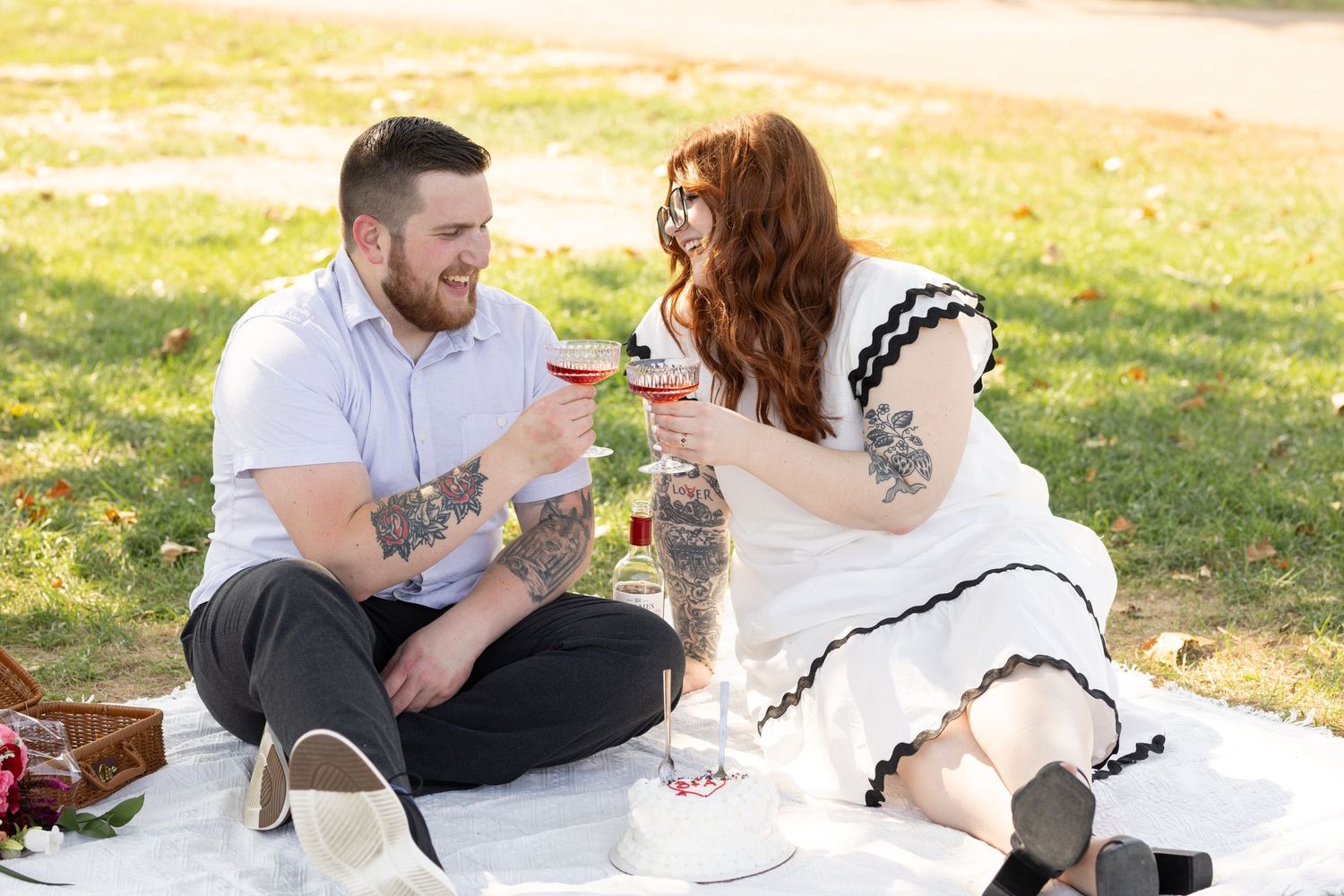 Couple enjoying wine during romantic picnic on white blanket in sunny park.