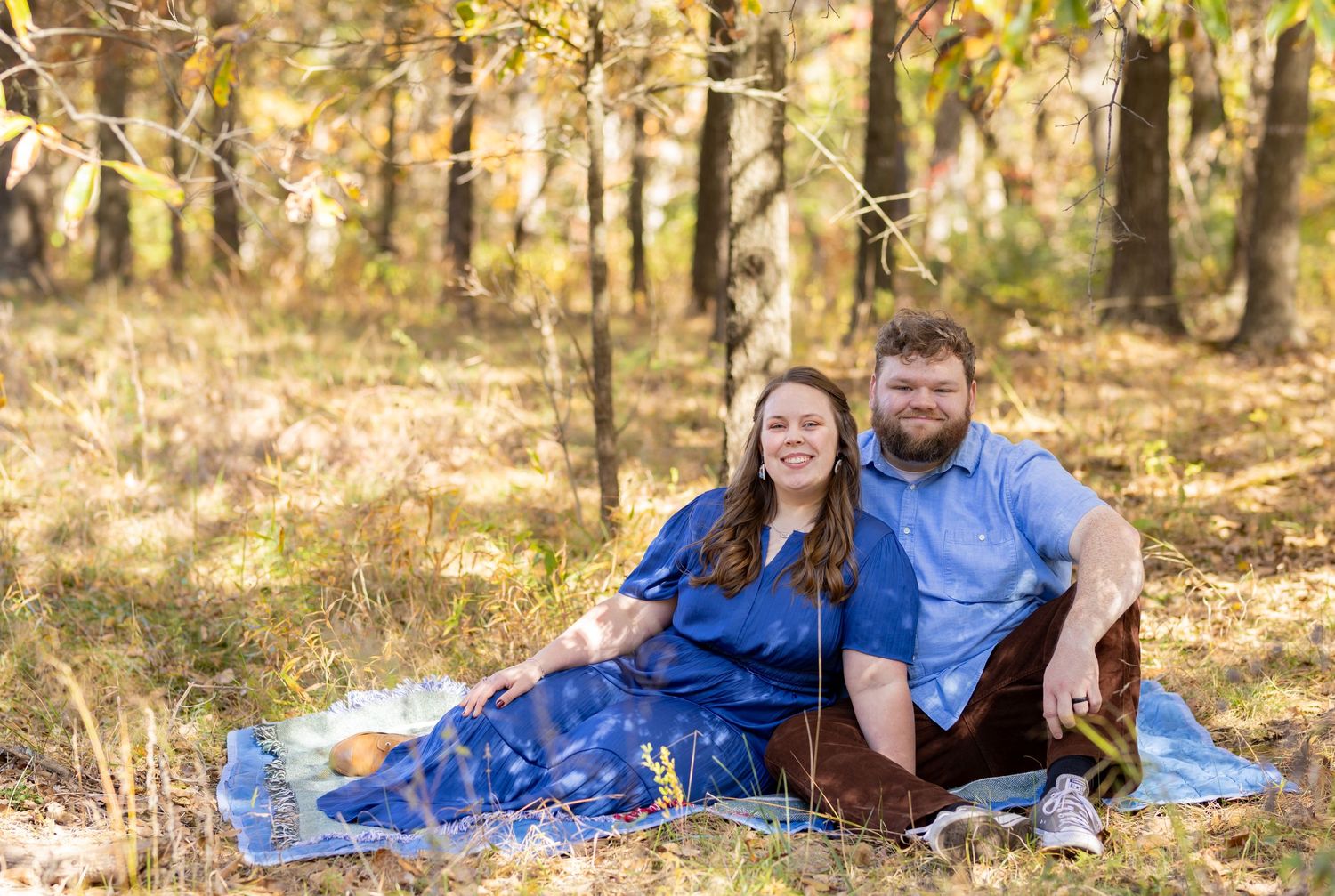 Couple relaxing on blanket during autumn photoshoot in wooded area.