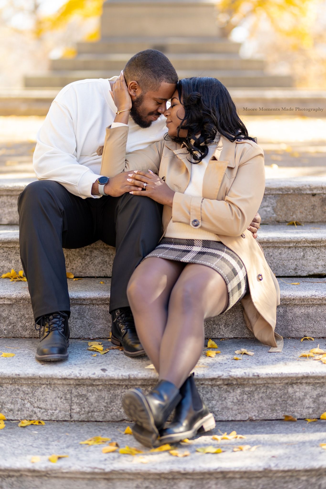 A couple sharing a romantic moment while sitting on stone steps surrounded by autumn leaves.