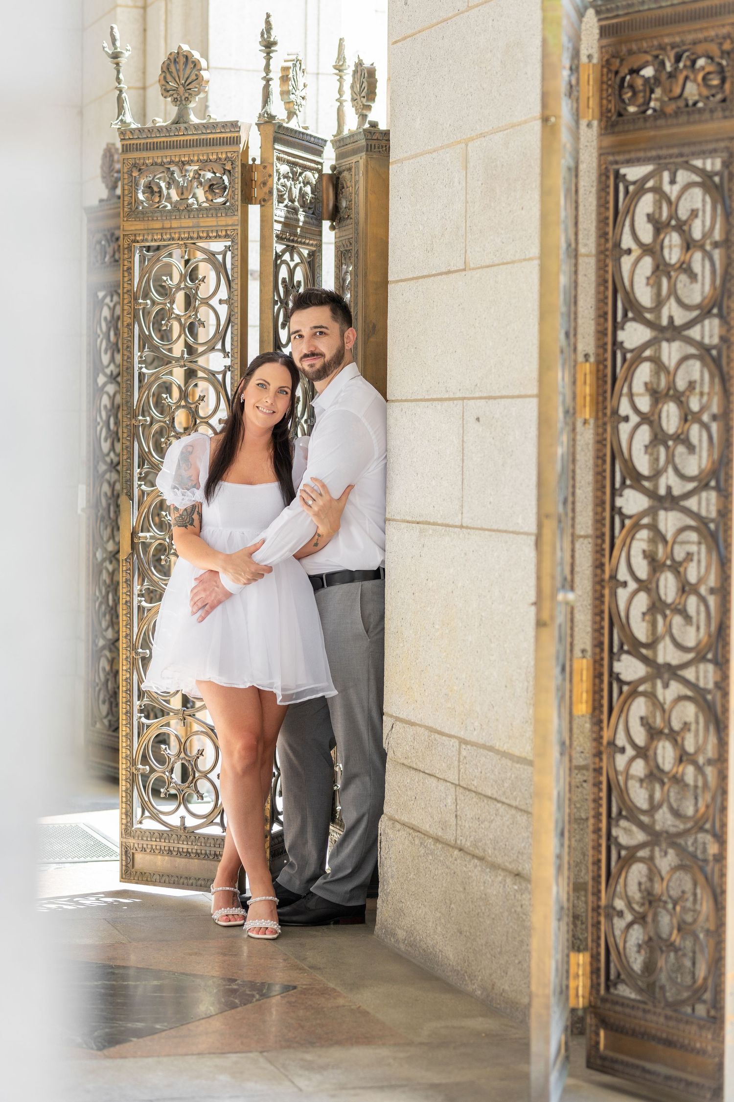 A couple poses together in an ornate hallway with decorative metalwork gates.