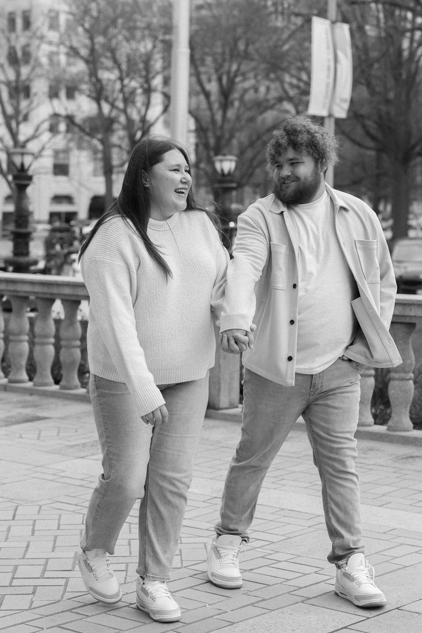 A couple shares a lighthearted moment together on a city street in black and white.