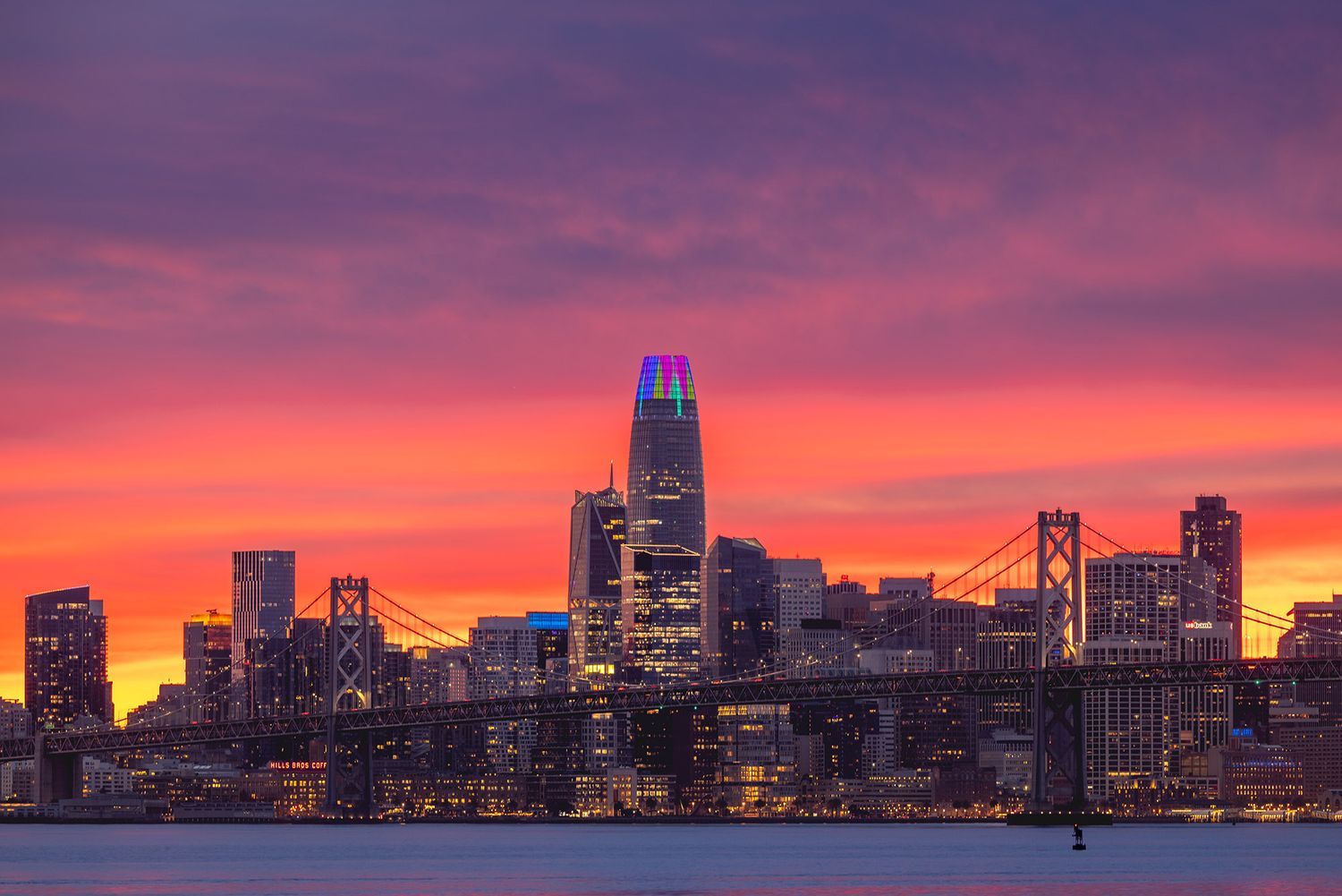 San Francisco skyline at sunset with vibrant pink and orange sky, Bay Bridge, and illuminated skyscrapers reflected over the bay.