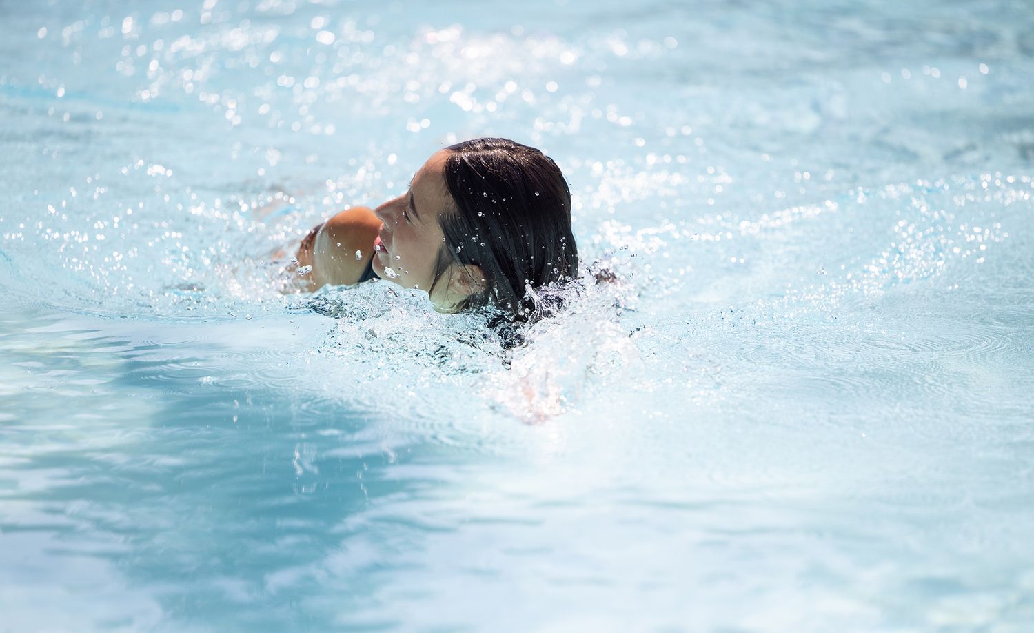 Child swimming freestyle stroke in a bright blue pool, splashing water around their head.