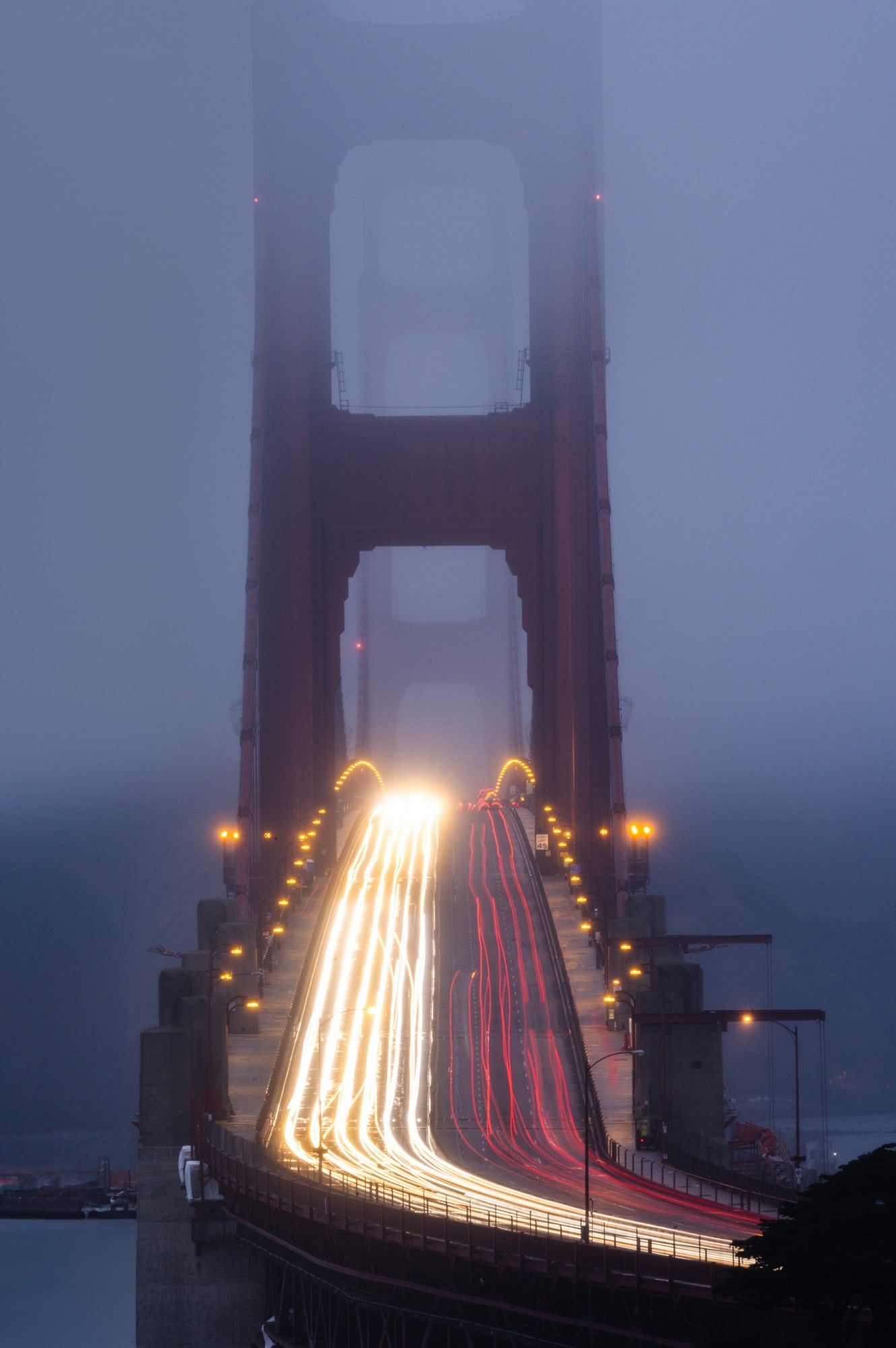 Long exposure photo of Golden Gate Bridge at night with light trails from traffic, shrouded in fog, San Francisco.