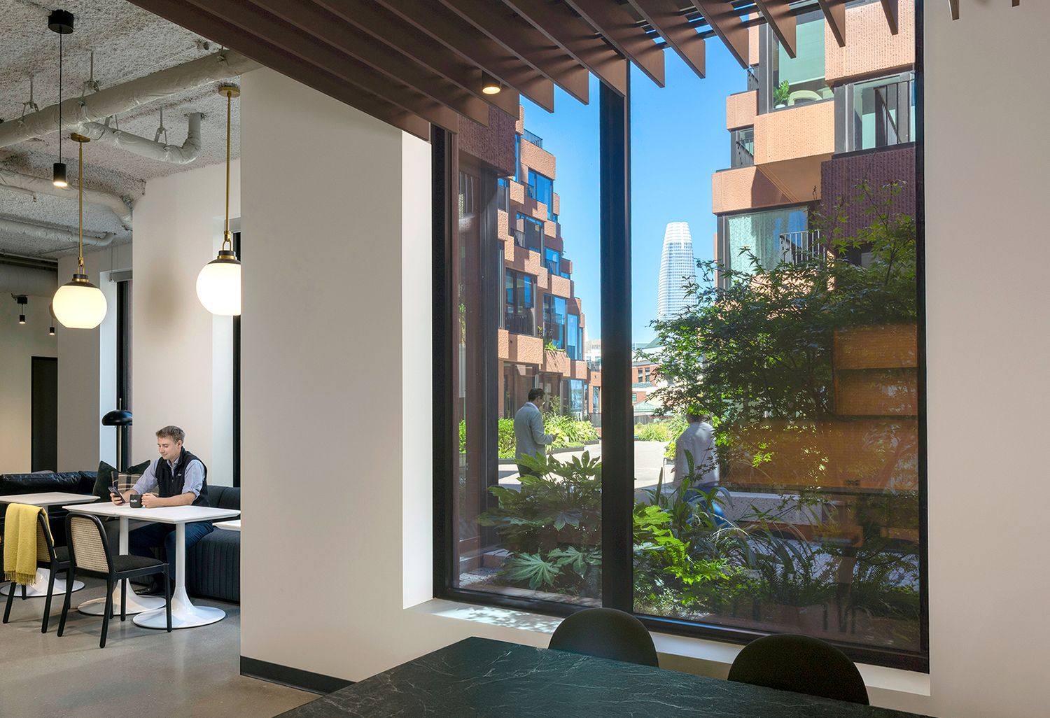 Stylish office interior with wooden slat ceiling, floor-to-ceiling windows overlooking a colorful urban building and greenery.