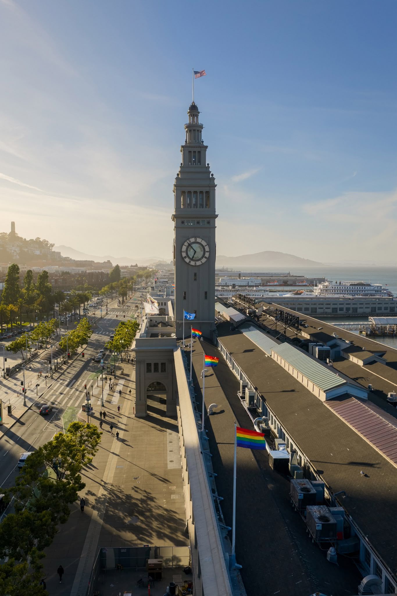 Aerial view of San Francisco Ferry Building clock tower with rainbow pride flags and bay views on a sunny day.