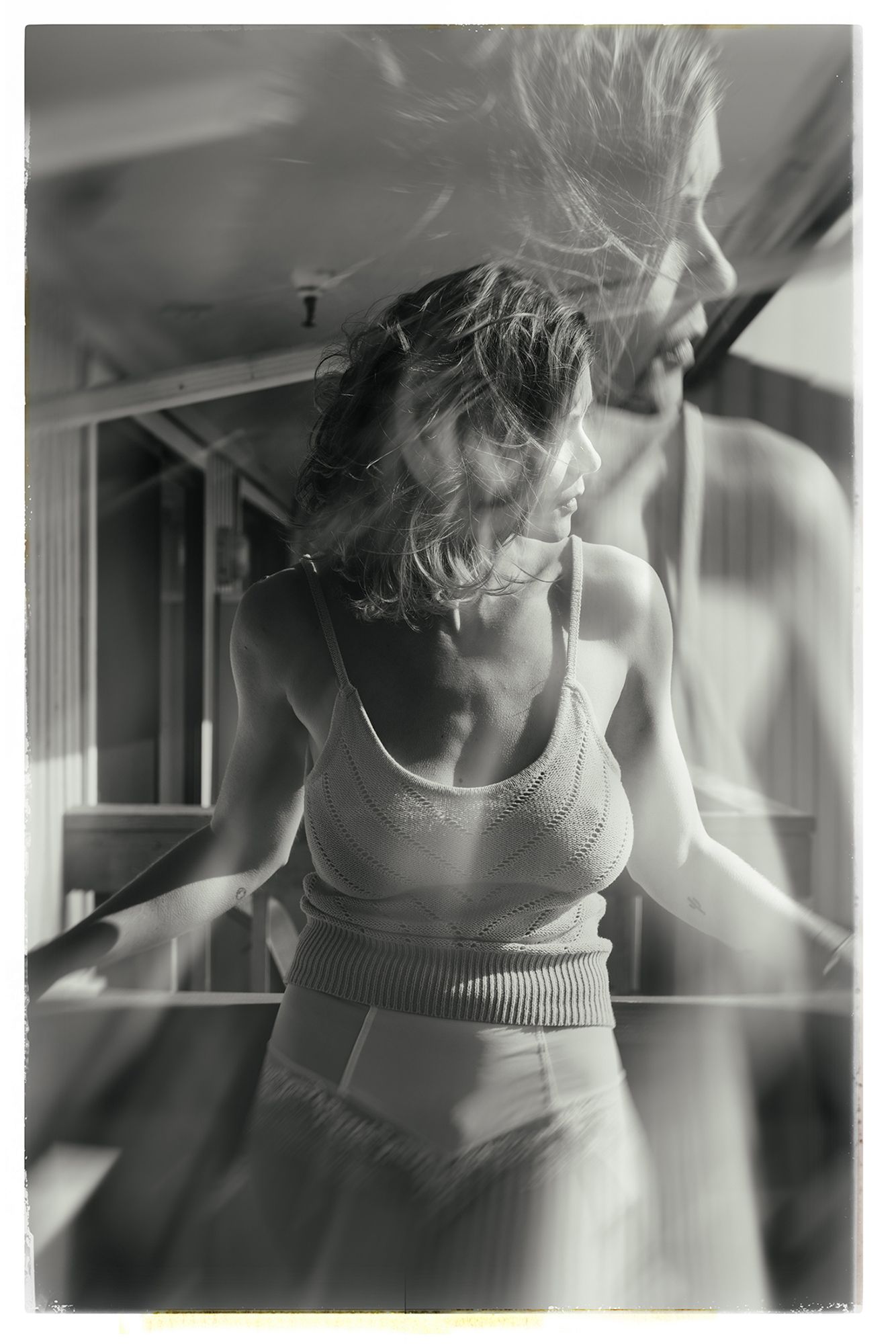Black and white photo of a woman in a knit crop top and pants, hair blowing, standing near a vehicle.