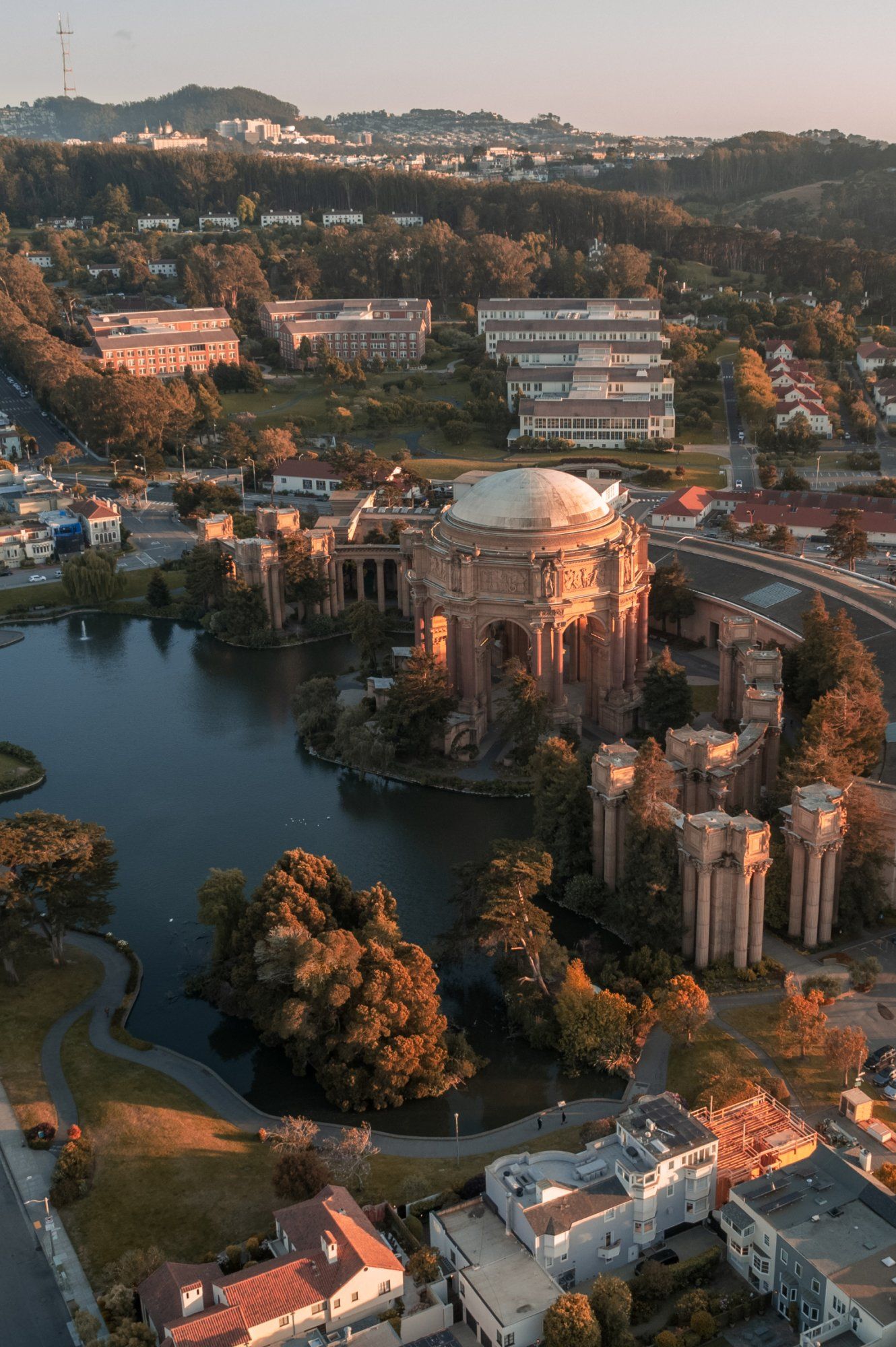 Aerial sunset view of the Palace of Fine Arts rotunda surrounded by lagoon and trees in San Francisco.