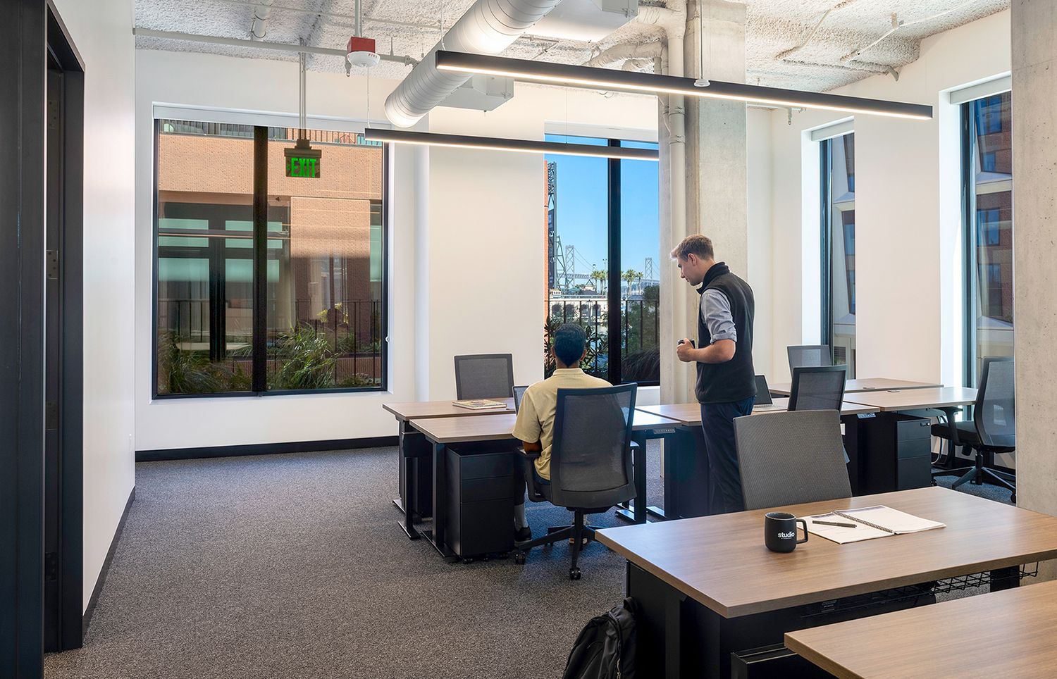 Modern open-plan office space with large windows, ergonomic chairs, and employees working at standing desks.