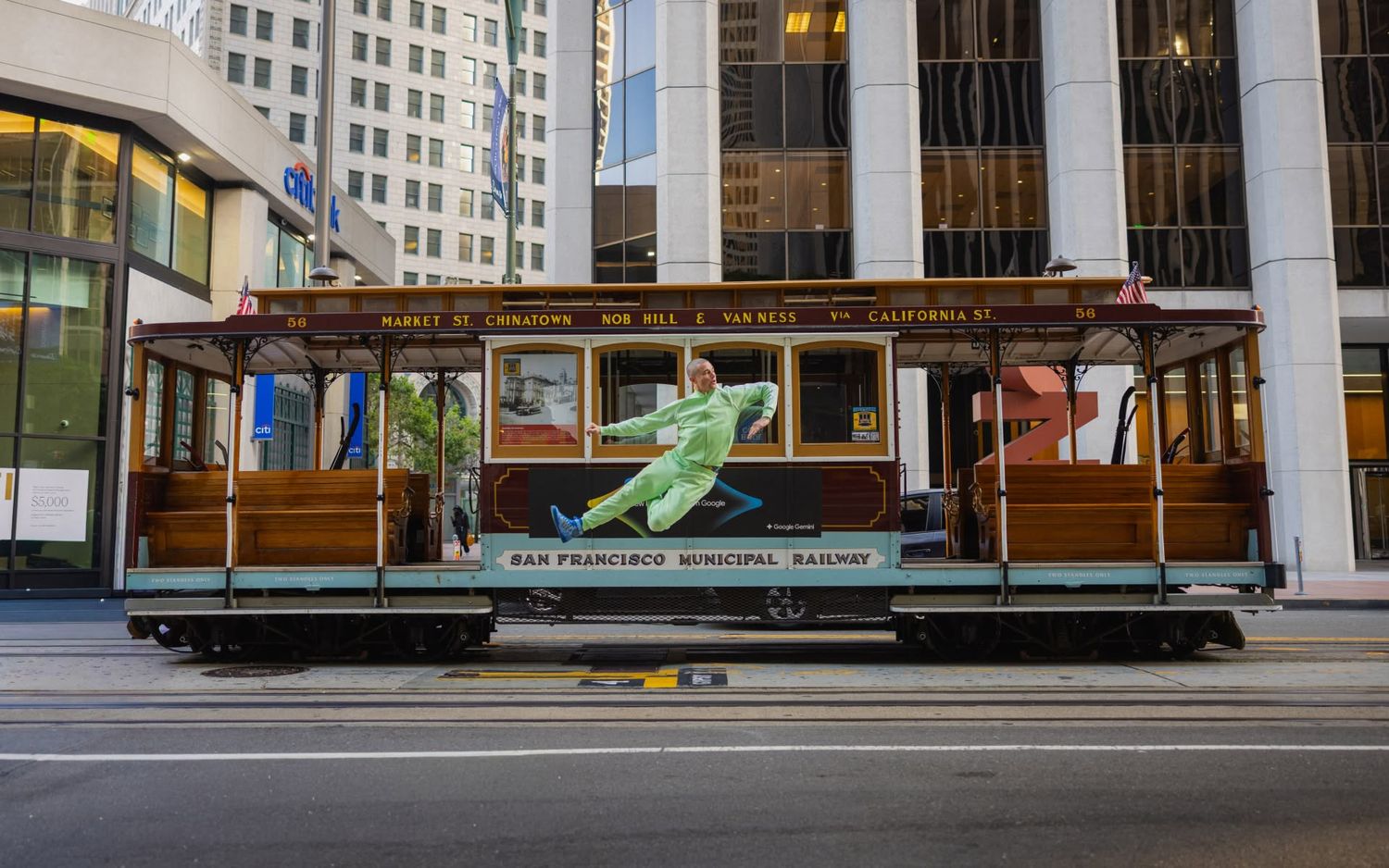 San Francisco Municipal Railway vintage cable car on city street with green figure advertisement on the side.