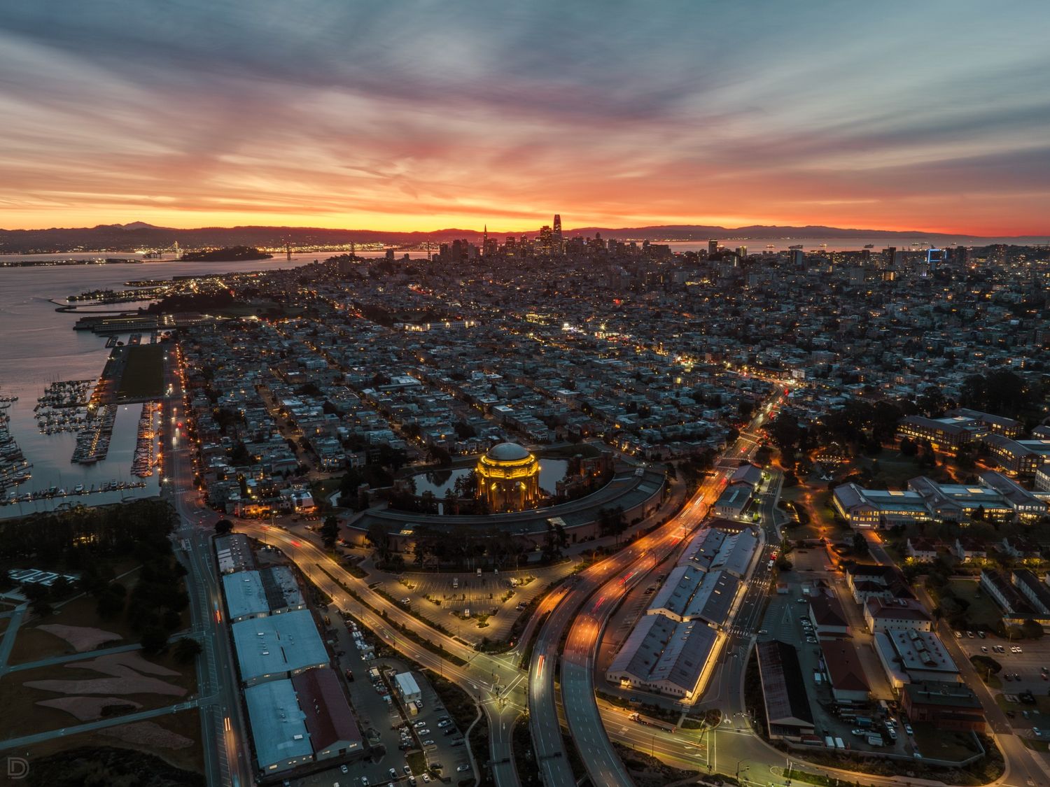 Aerial panoramic view of San Francisco cityscape glowing under a vibrant red and orange sunset sky.
