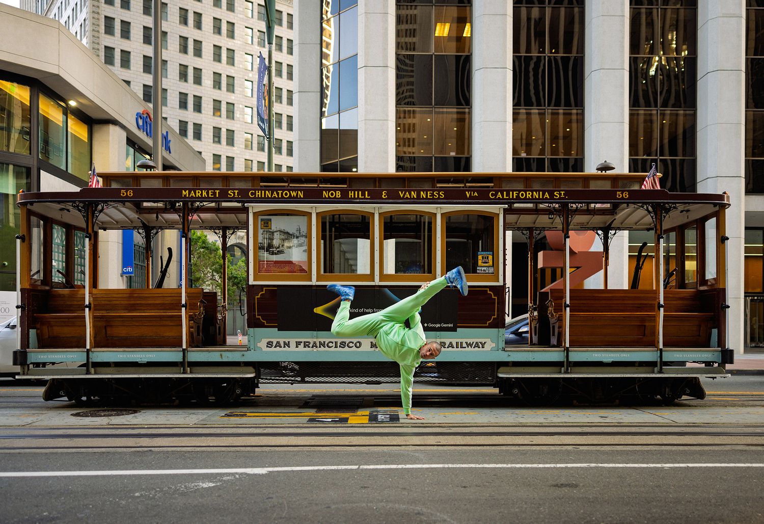 A green figure breakdancing in front of a classic San Francisco cable car on a city street.