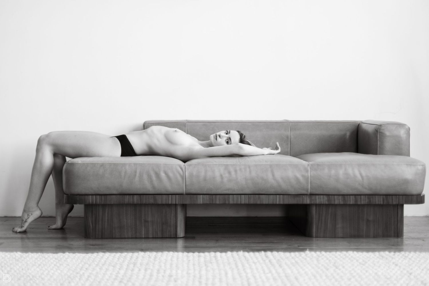 Black and white artistic photo of a woman reclining on a modern gray sofa in minimalist interior.