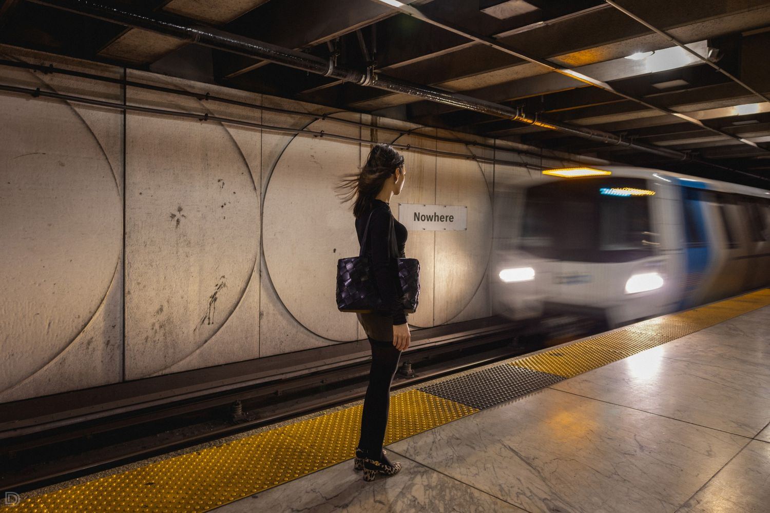Woman standing on subway platform as a blurred metro train arrives at the station.