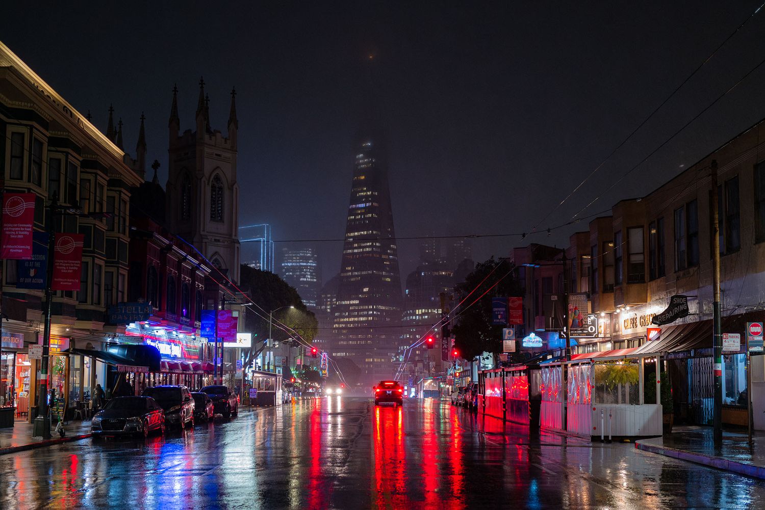 Rainy night street scene with colorful neon reflections and a glowing skyscraper in the foggy distance.