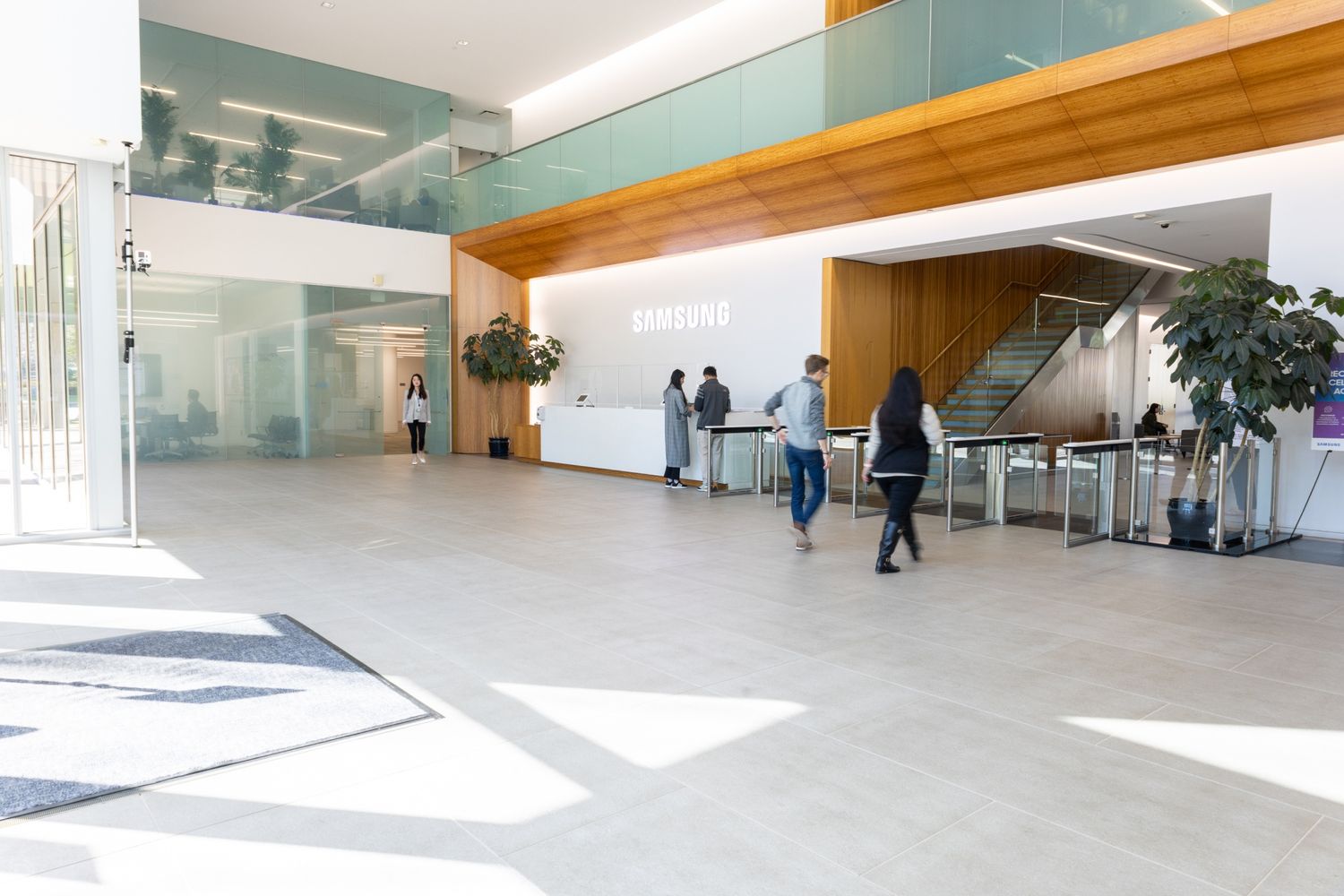 Modern corporate office lobby with reception desk, turnstiles, wood accents, and natural light.