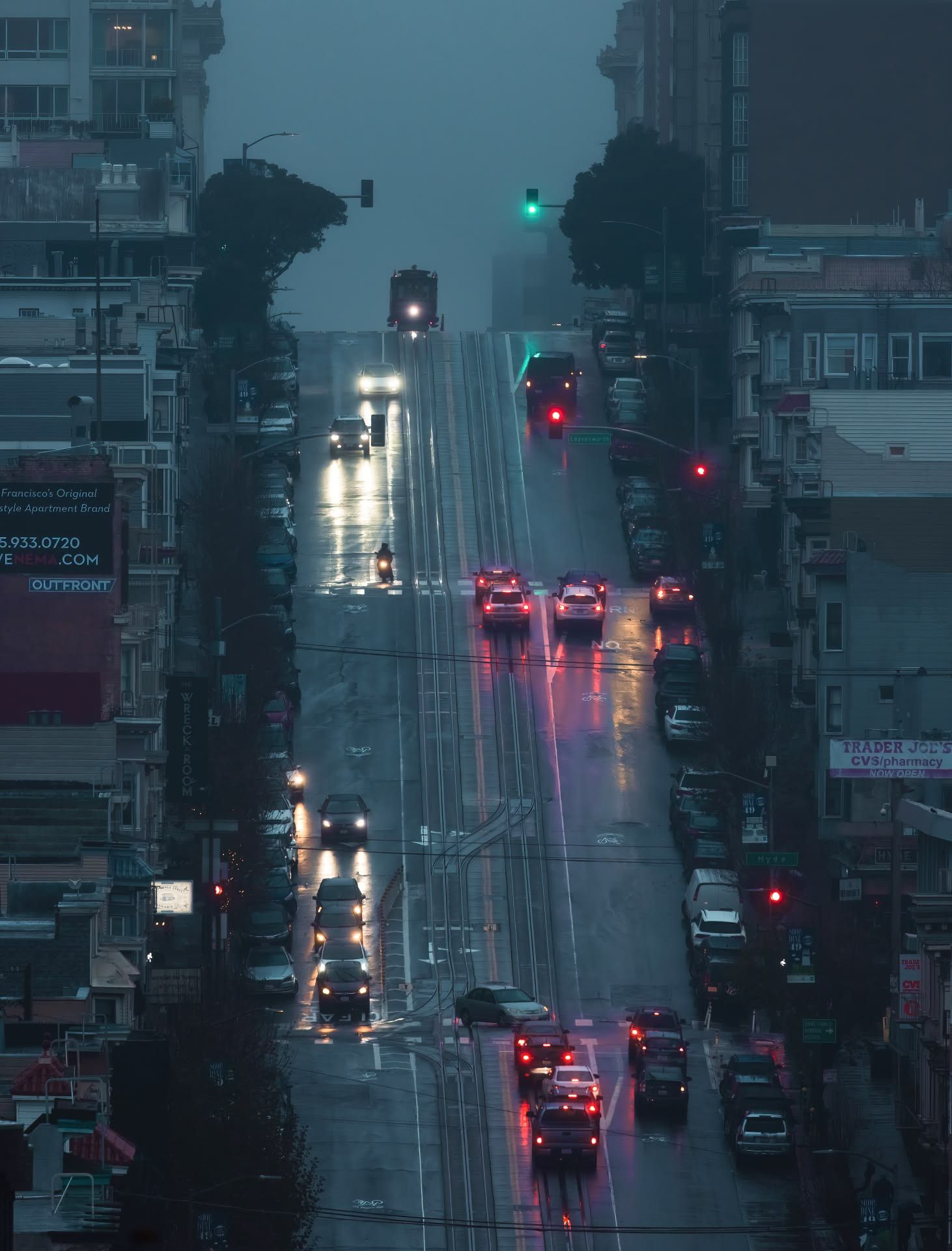 Rainy night city street with glowing red and white car lights reflecting on wet pavement.