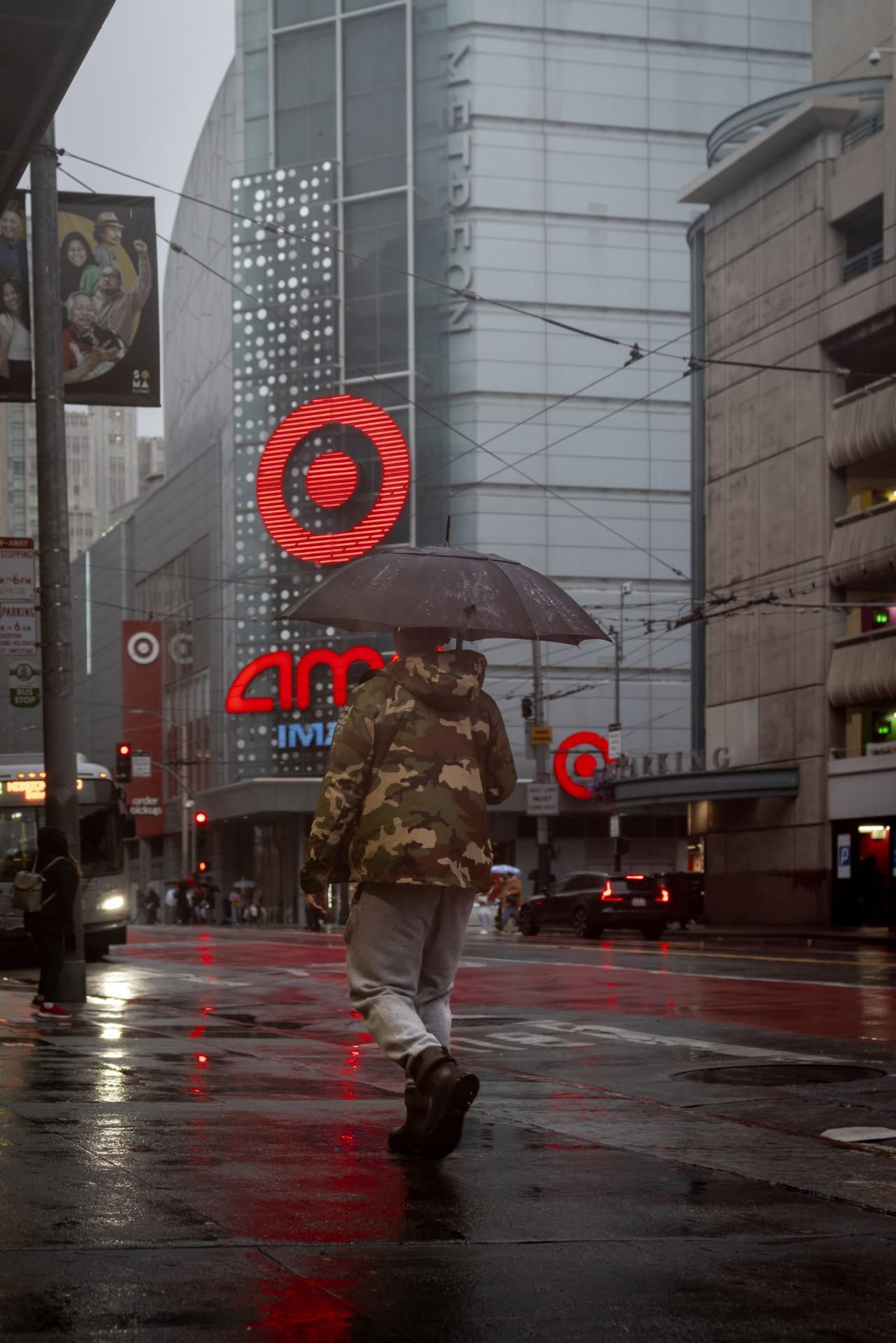Person walking with umbrella on a rainy city street past a glowing Target store sign.