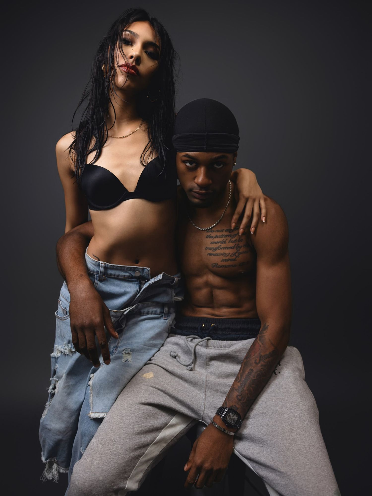 Athletic couple posing together in casual streetwear against a dark studio background.