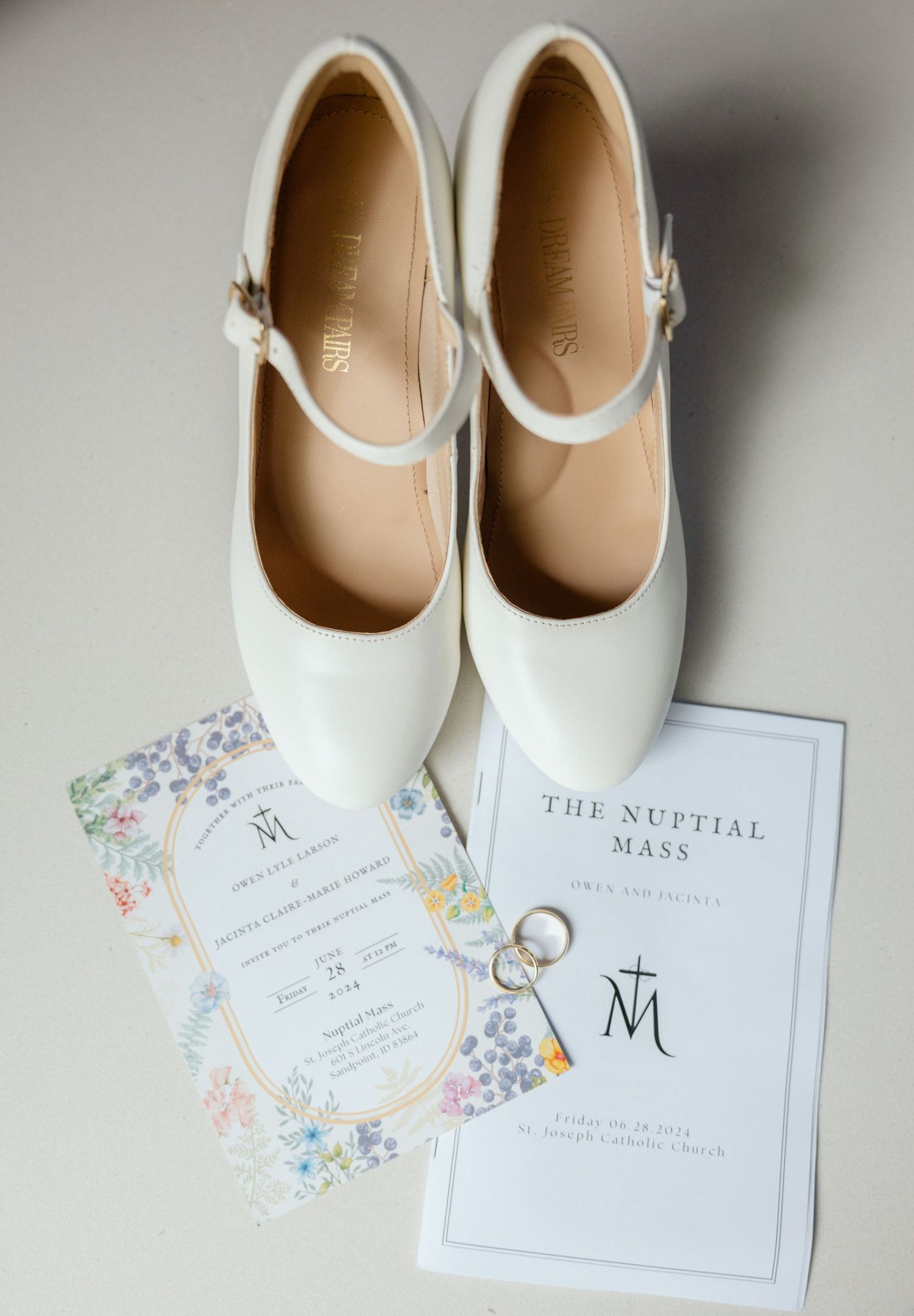 An elegantly styled wedding detail shot featuring elegant white high heels, sparkling wedding rings, and whimsical wedding invitations.