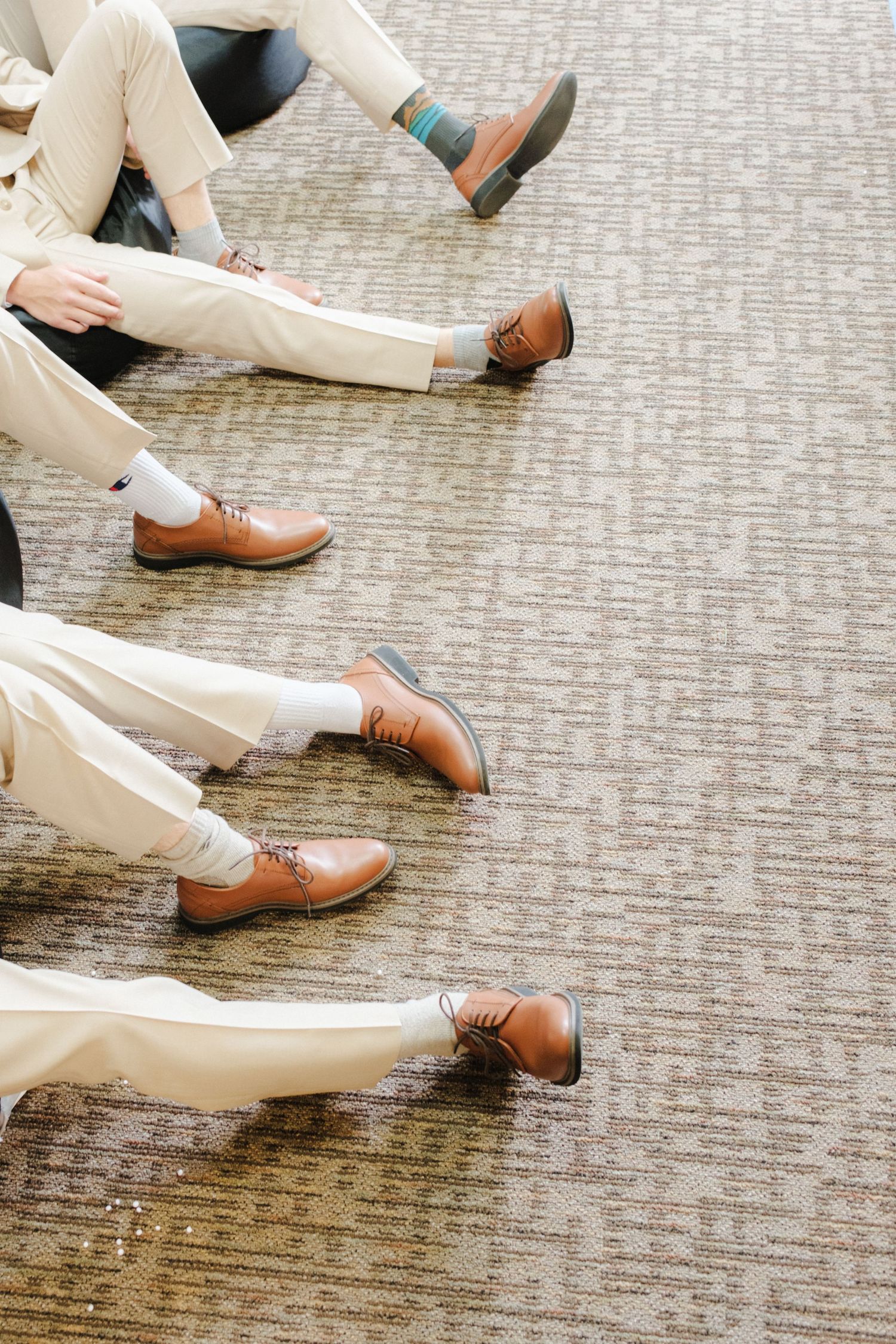Groomsmen's lower legs and polished shoes in cream suits, sitting on the floor in a stylish and coordinated wedding look.