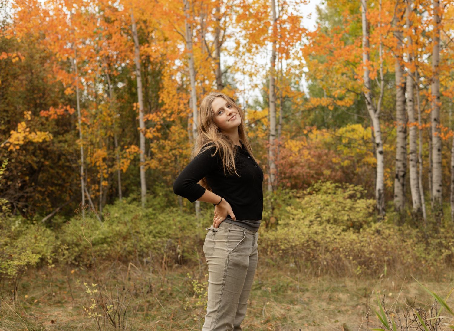 Confident woman posing in golden autumn woods, surrounded by vibrant fall leaves, reflecting warmth, natural beauty, calm and joy.