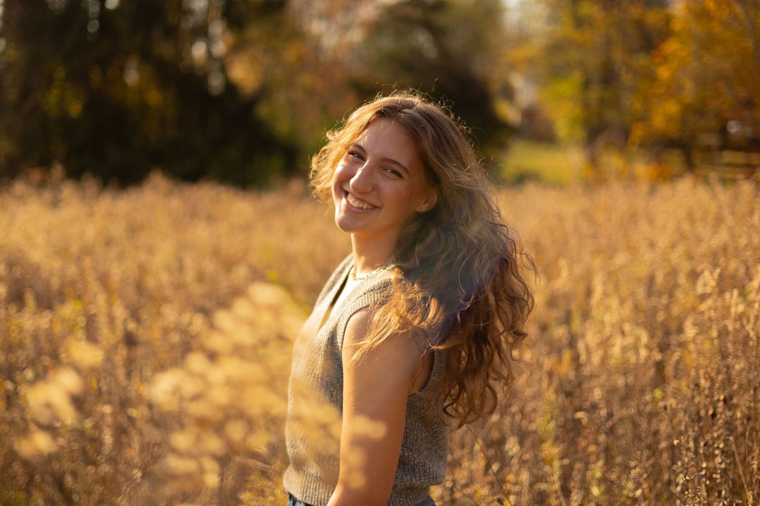 Smiling young woman in a sunlit golden field, embracing the warmth of autumn with natural beauty and radiant joy.