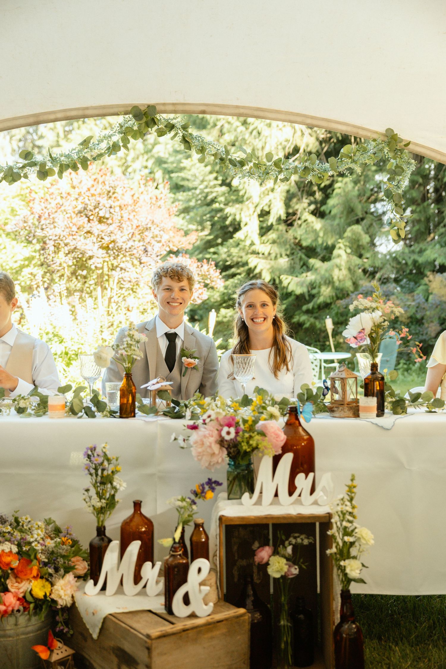 Bride and Groom sitting at a decorated wedding table under a tent, with flowers and 